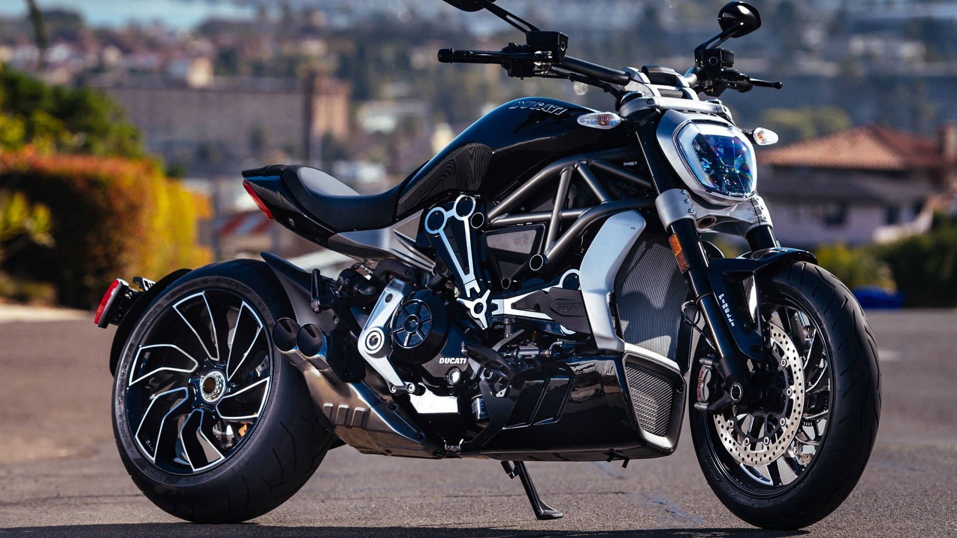 機車 桌布 壁紙 — 一台時尚黑色Ducati機車，帶有外露的銀色車架和複雜的機械細節，停放在陽光明媚的街道上。
