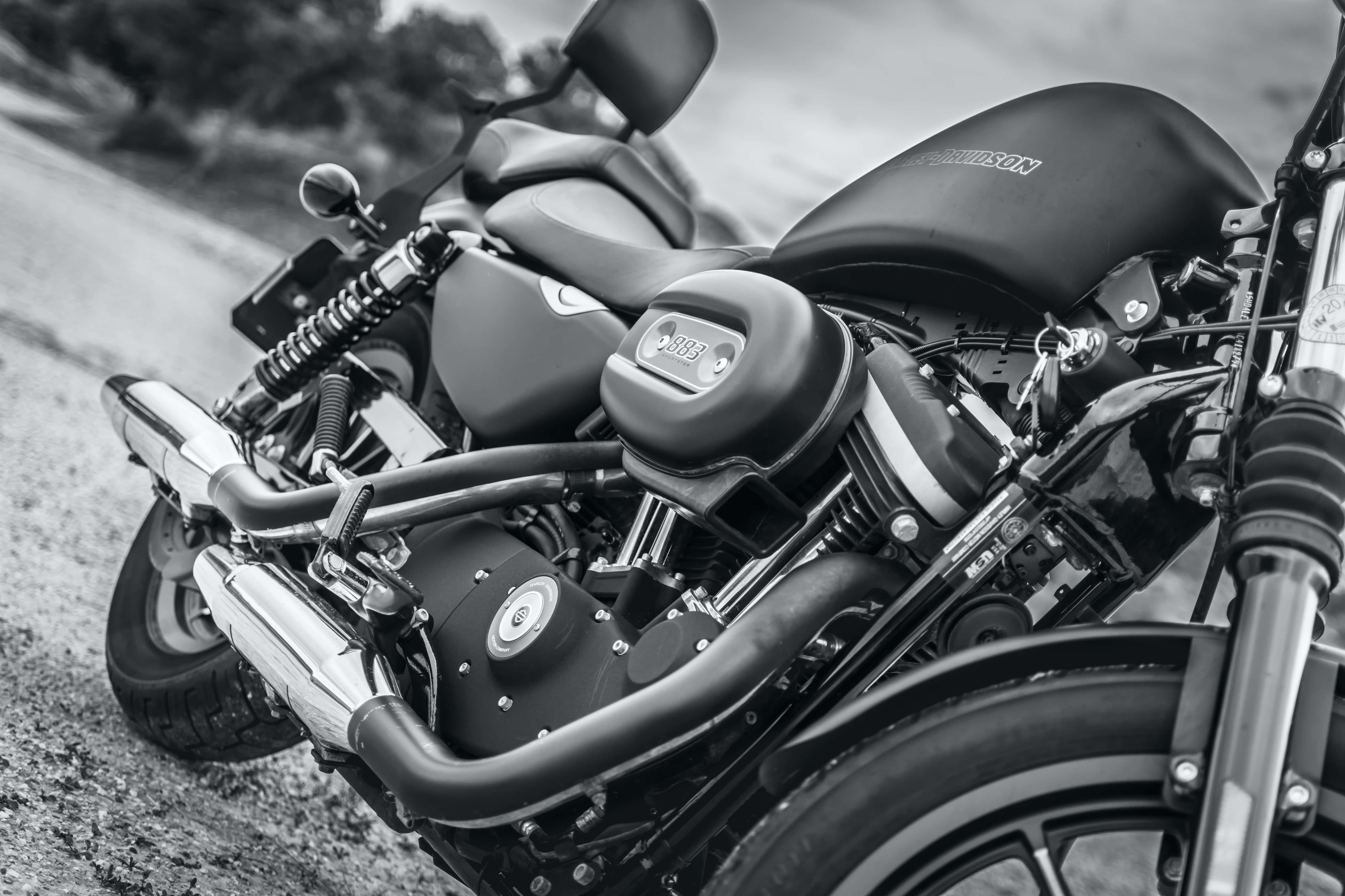 Harley Davidson HD 桌布 壁紙 — 一台時尚黑色Harley-Davidson機車停在碎石路上，背景有模糊的樹木。