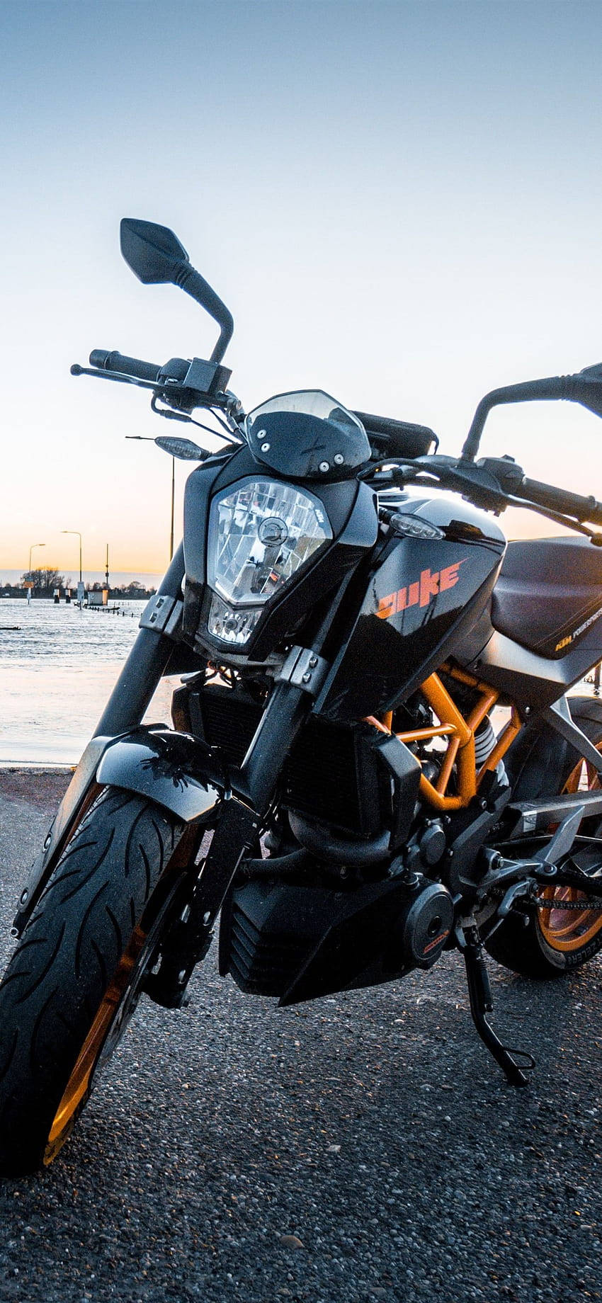 機車 桌布 壁紙 — 一台時尚黑色KTM Duke機車帶橙色點綴，停放在日落時分近水邊的柏油路上。
