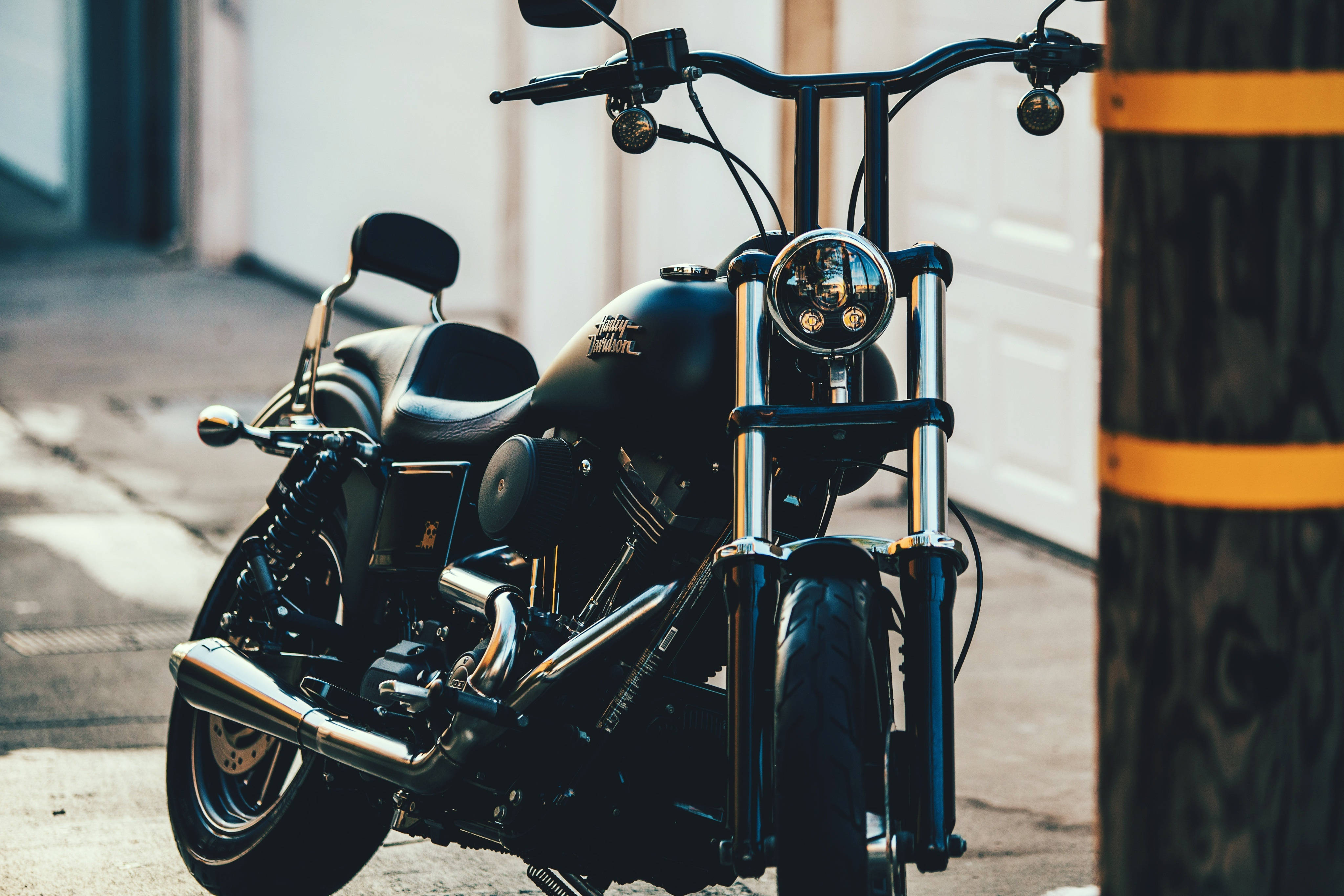 Harley 桌布 壁紙 — 一台時尚黑色機車，帶有鍍鉻裝飾，停放在陽光普照的城市人行道上，旁邊有一根帶黃色條紋的木柱。