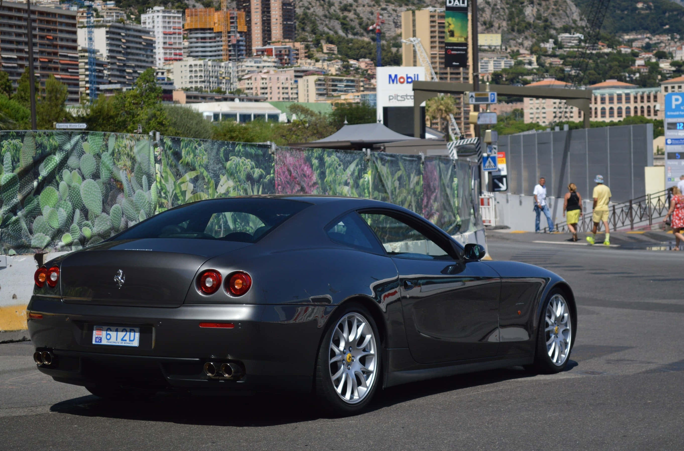Ferrari 612 Scaglietti 桌布 壁紙 — 一台時尚黑色法拉利跑車停放在陽光普照的城市街道上，背景是城市天際線和仙人掌圍欄。