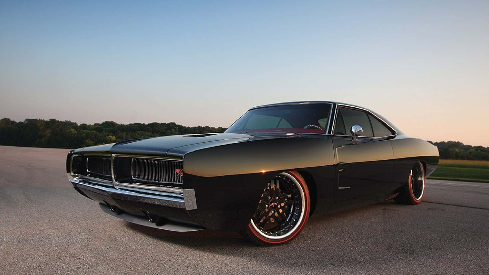 Dodge Charger 桌布 壁紙 — 一台時尚黑色經典肌肉車，配紅色輪圈，在日落光線下於開闊道路上閃閃發光。