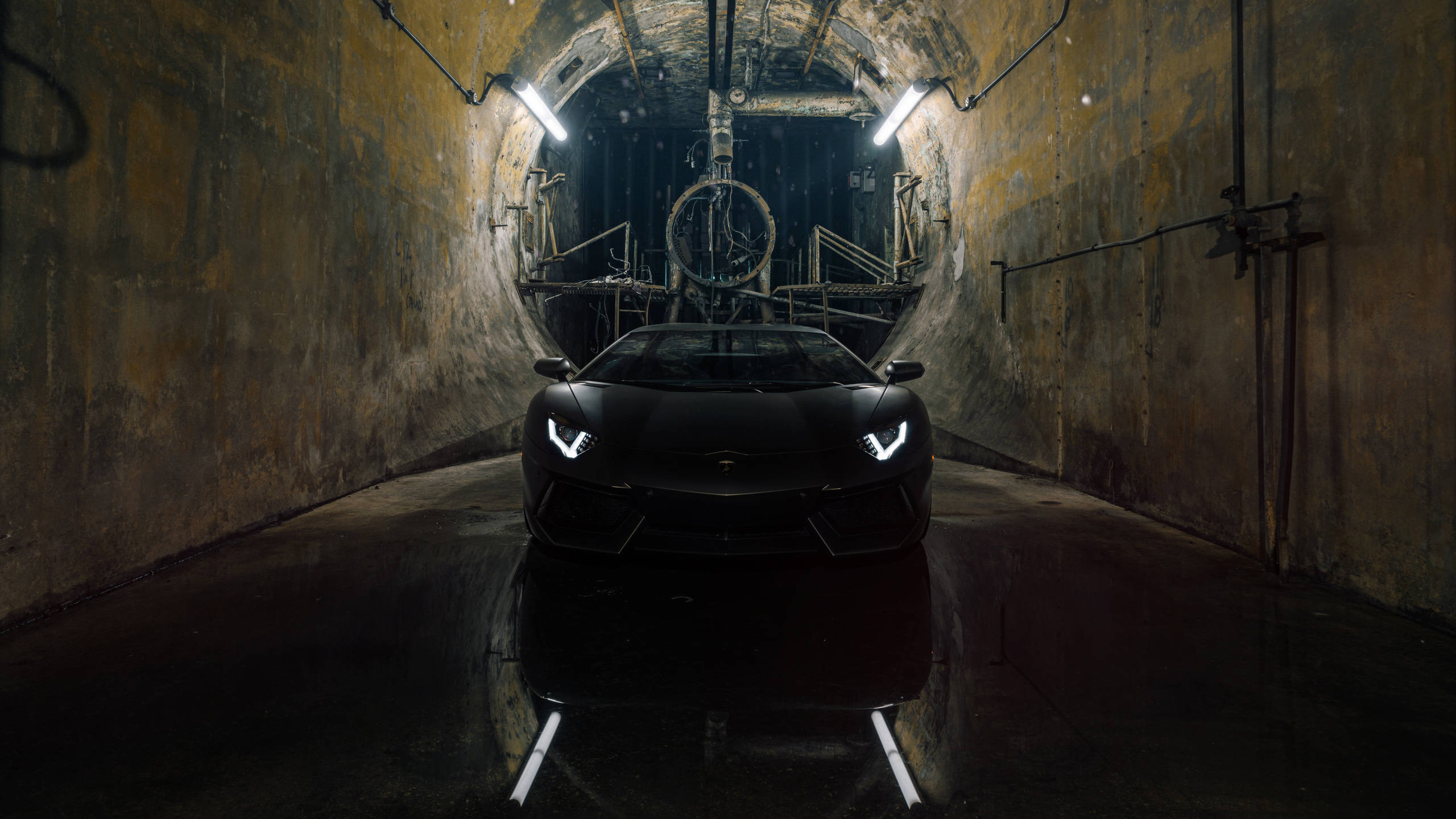 Lamborghini 4K 桌布 壁紙 — 一台時尚黑色藍寶堅尼 Aventador 停在燈光昏暗的工業隧道中央，地面潮濕反光，管線外露。