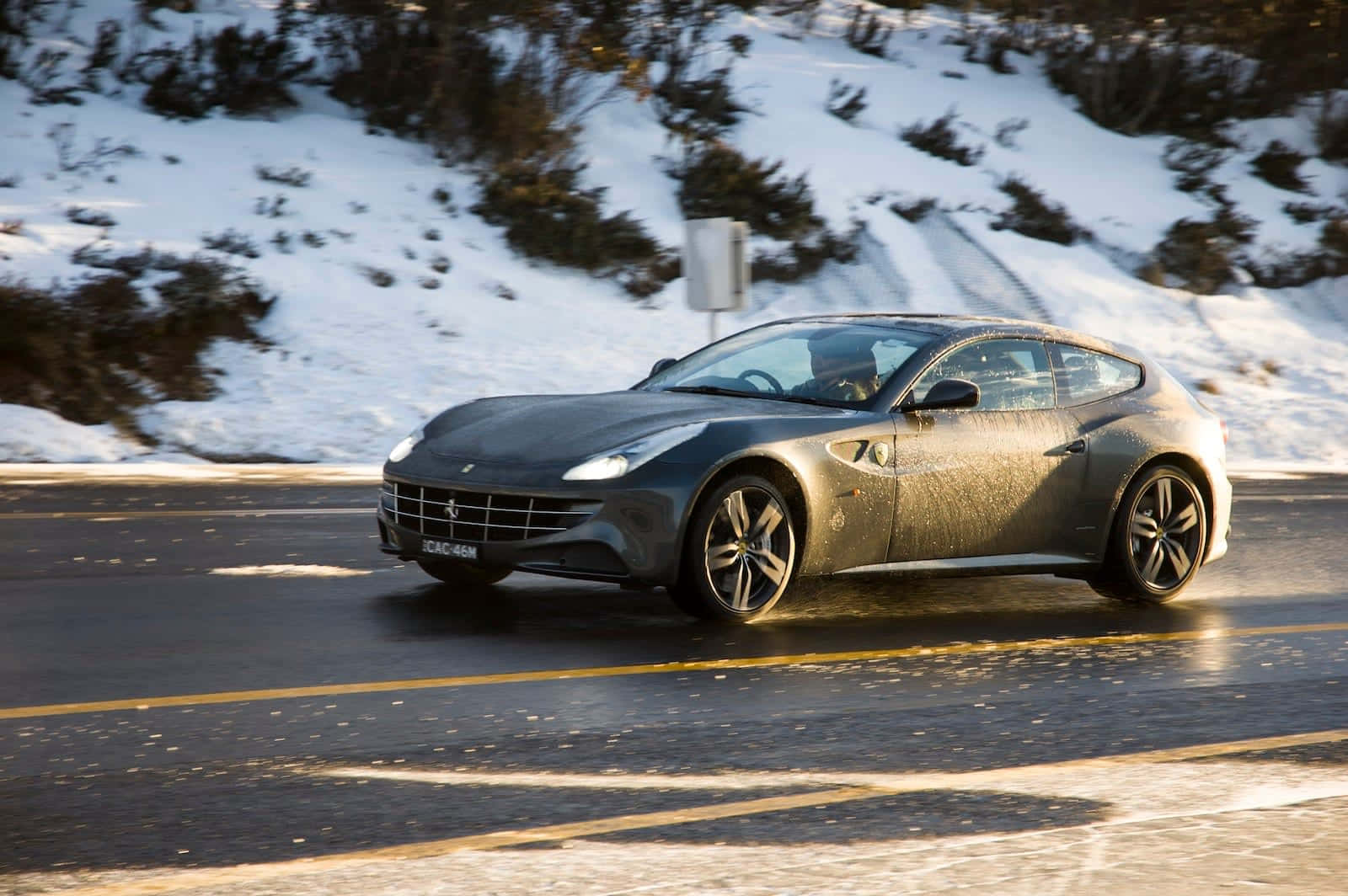 Ferrari Ff 桌布 壁紙 — 一台流線型灰色法拉利在白雪覆蓋的山路上行駛，背景是陽光普照的雪山丘陵。
