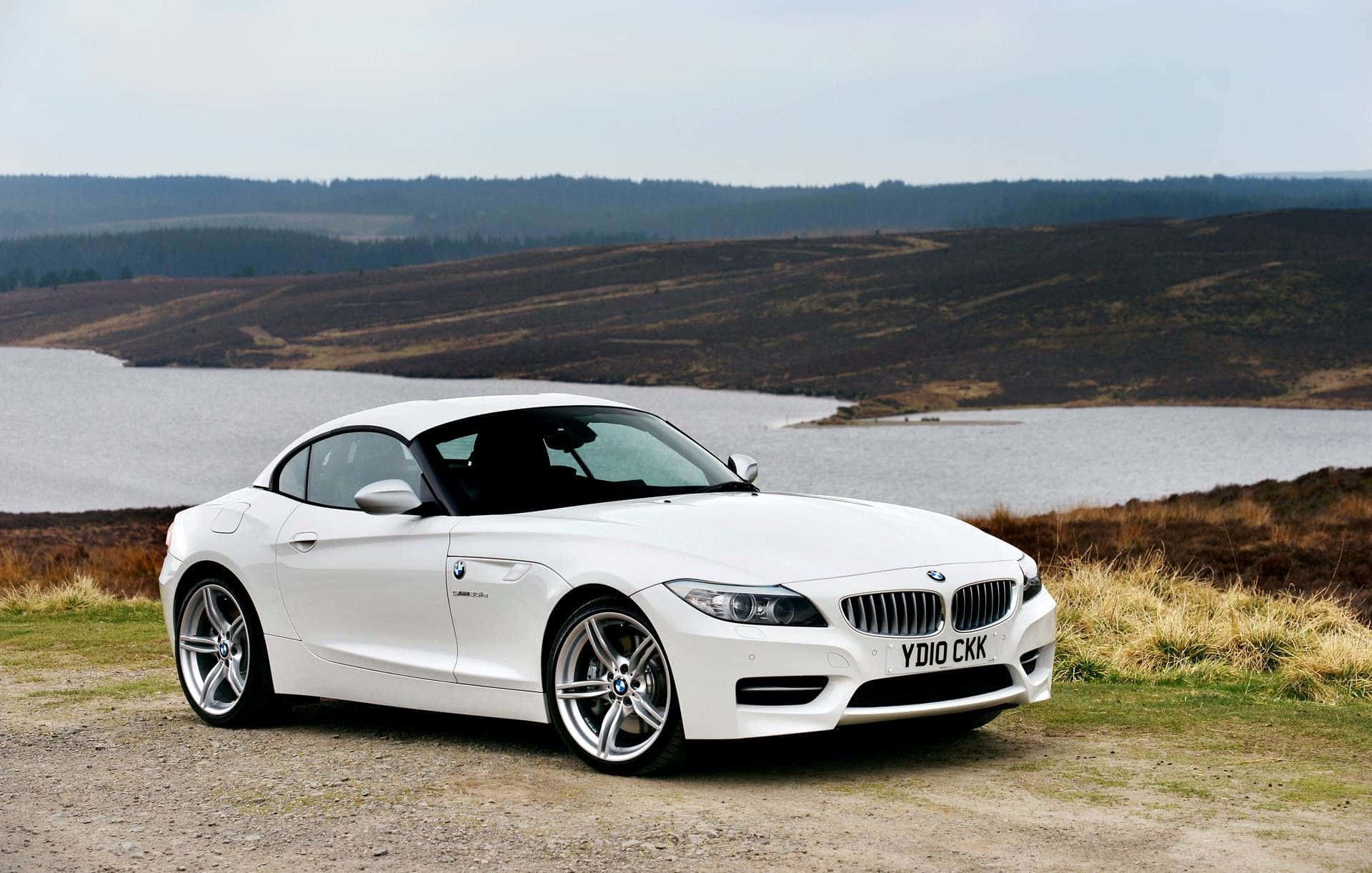 Bmw Z4 桌布 壁紙 — 一台流線型白色BMW Z4敞篷跑車停放在青草山坡上，俯瞰平靜湖泊，背景是起伏的荒野丘陵。