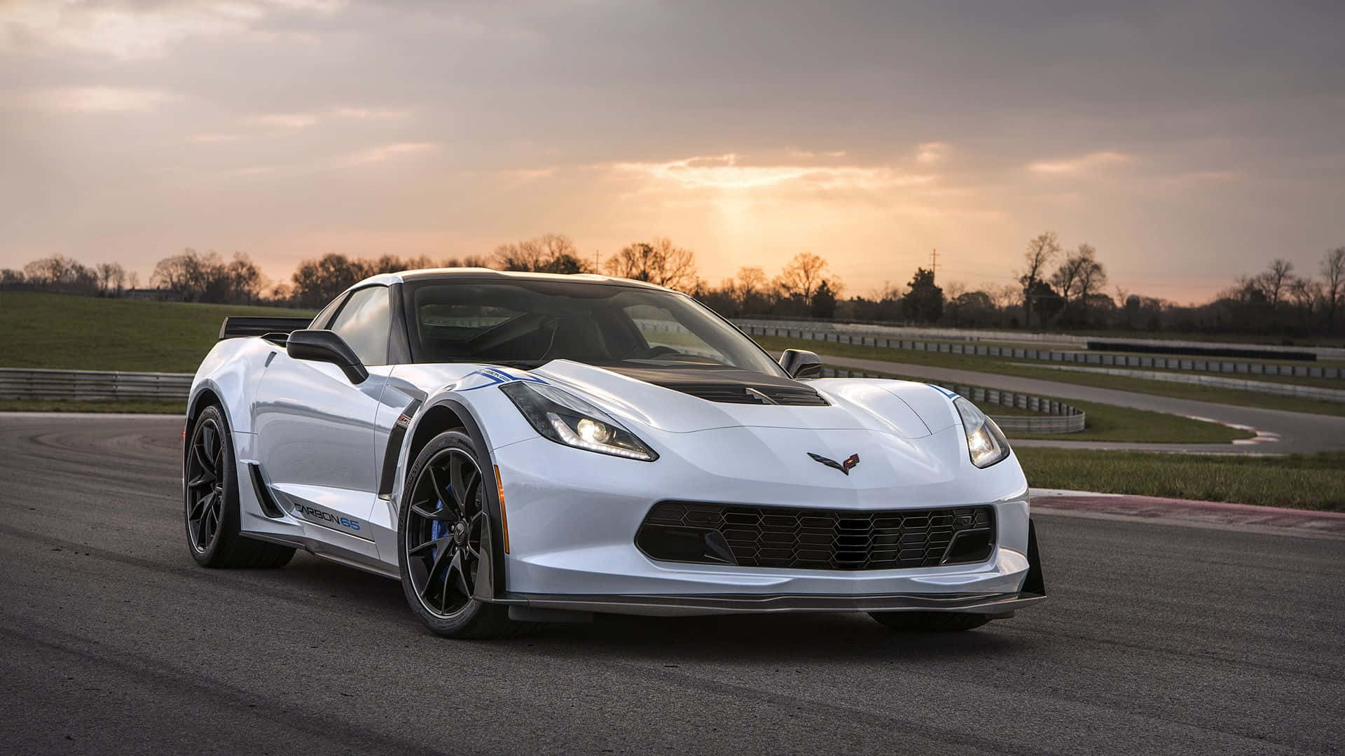 corvette 桌布 壁紙 — 一台流線型白色Corvette跑車在日落時分沿著蜿蜒的賽道滑行，溫暖的金色光芒投下長長的影子。