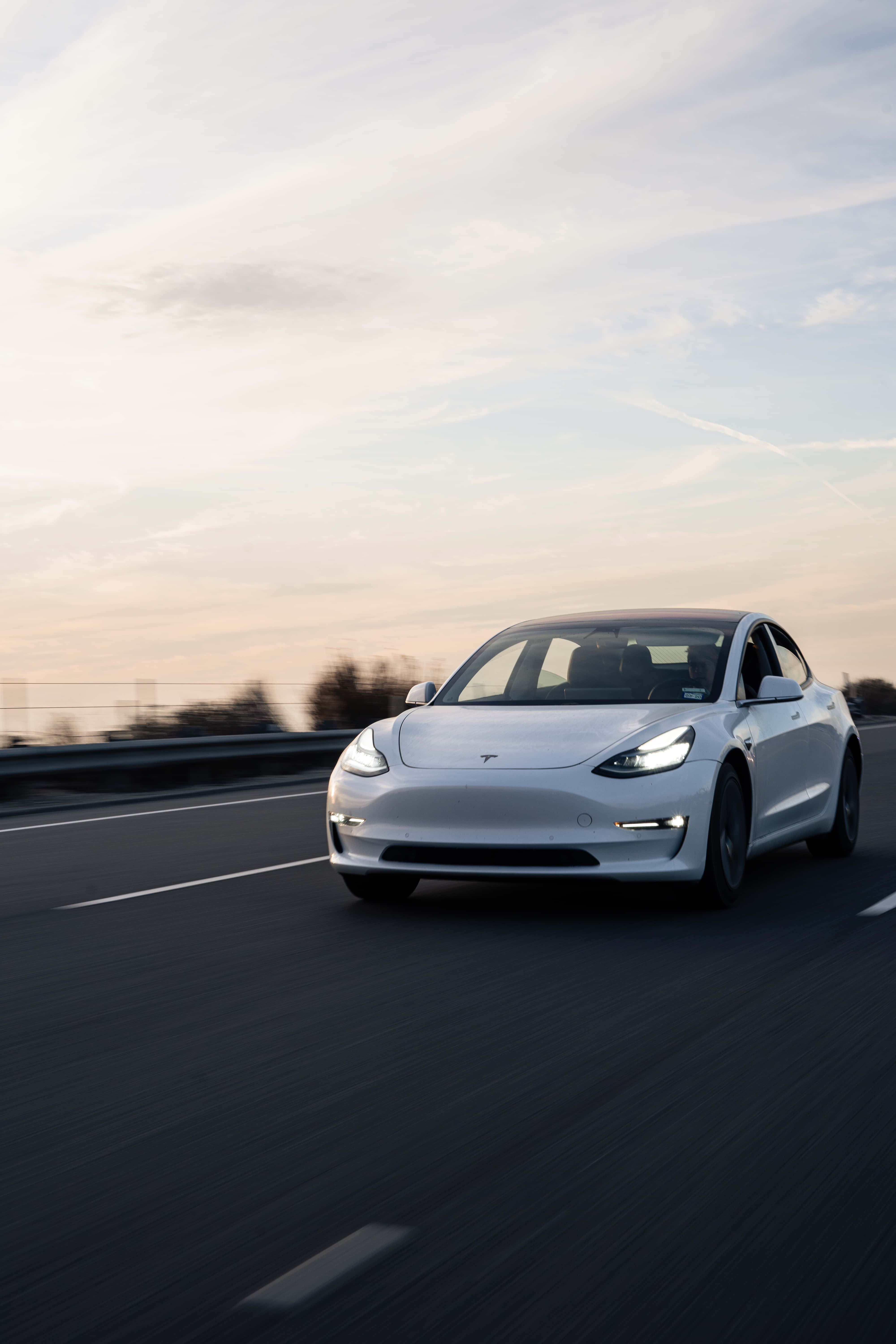 特斯拉 桌布 壁紙 — 一台流線型白色Tesla Model 3在柔和粉彩夕陽天空下沿高速公路疾駛，帶有模糊的動態線條。