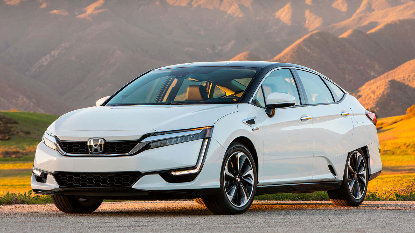 Honda Clarity 桌布 壁紙 — 一台流線型白色本田Clarity插電式混合動力轎車停泊在道路上，背景是陽光普照的起伏山丘和遠處的山脈。