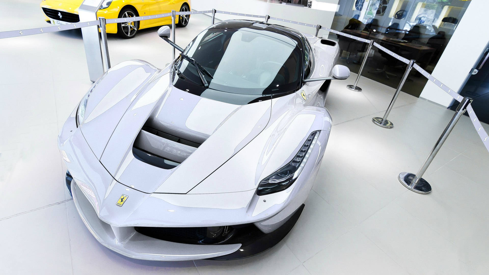 white ferrari 桌布 壁紙 — 一台流線型白色法拉利LaFerrari超級跑車在明亮燈光下閃耀，背景是黃色法拉利的豪華展廳。