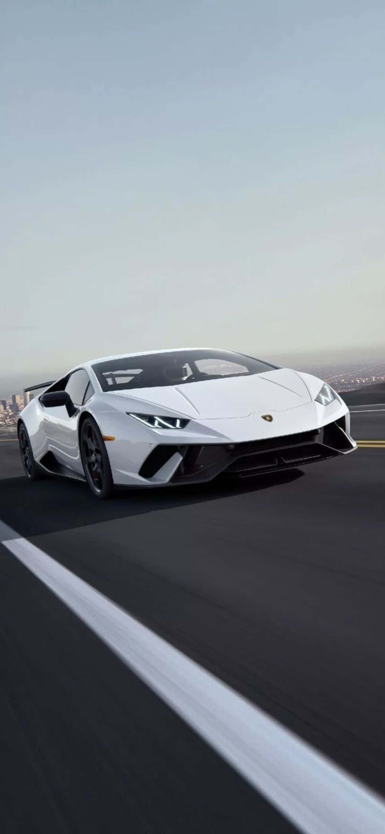 Lamborghini Phone 桌布 壁紙 — 一台流線型白色藍寶堅尼Huracán沿著海岸公路疾馳，遠方是朦朧的城市天際線。