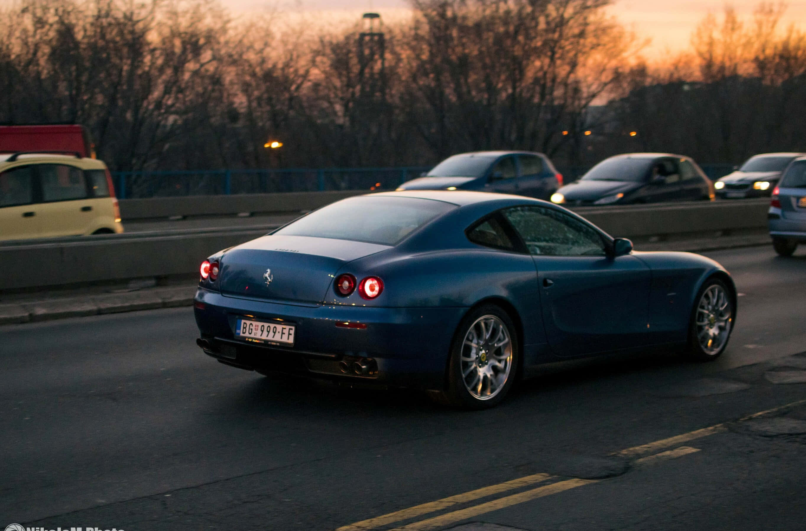 Ferrari 612 Scaglietti 桌布 壁紙 — 一台流線型的藍色法拉利612 Superamerica在日落時分於高速公路上行駛，尾燈閃爍，背景有光禿的樹木。