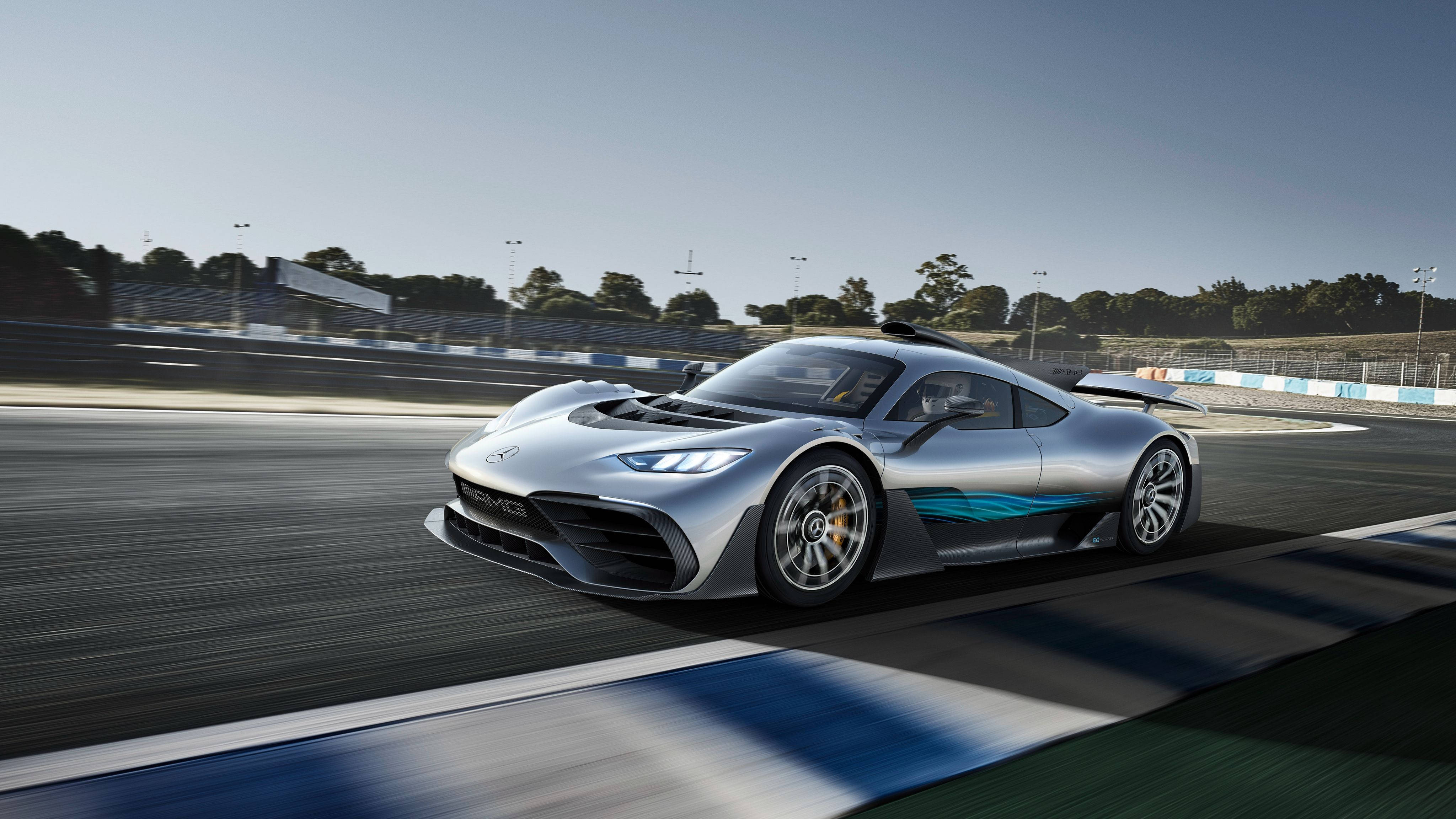cars 桌布 壁紙 — 一台流線型的銀色 Mercedes-AMG One 超跑在陽光明媚的賽道上疾馳，帶有模糊的動感和藍色點綴。