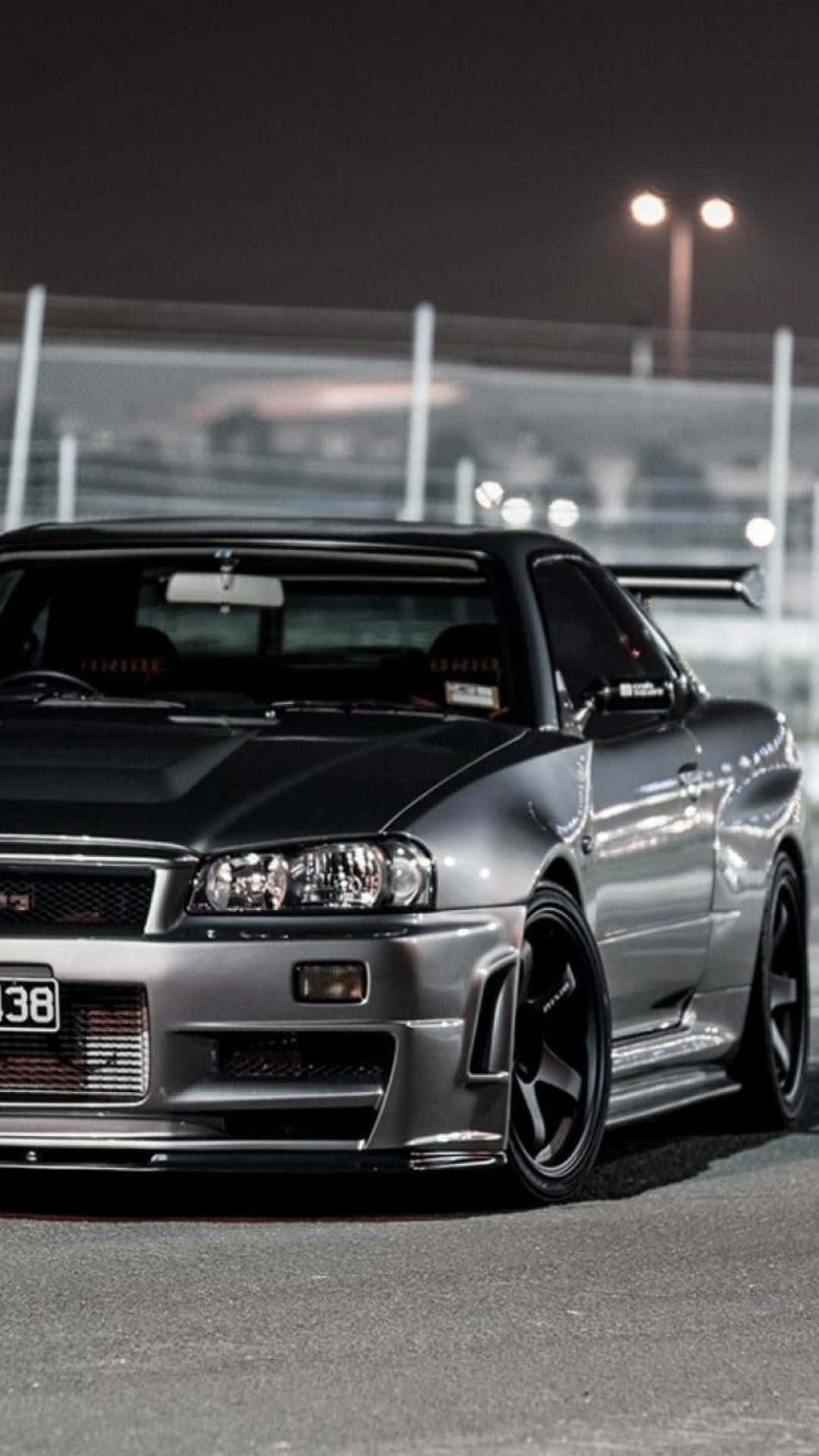 桌布 壁紙 — 一台流線型的銀色日產Skyline R34跑車在夜間賽道的燈光下閃閃發光。