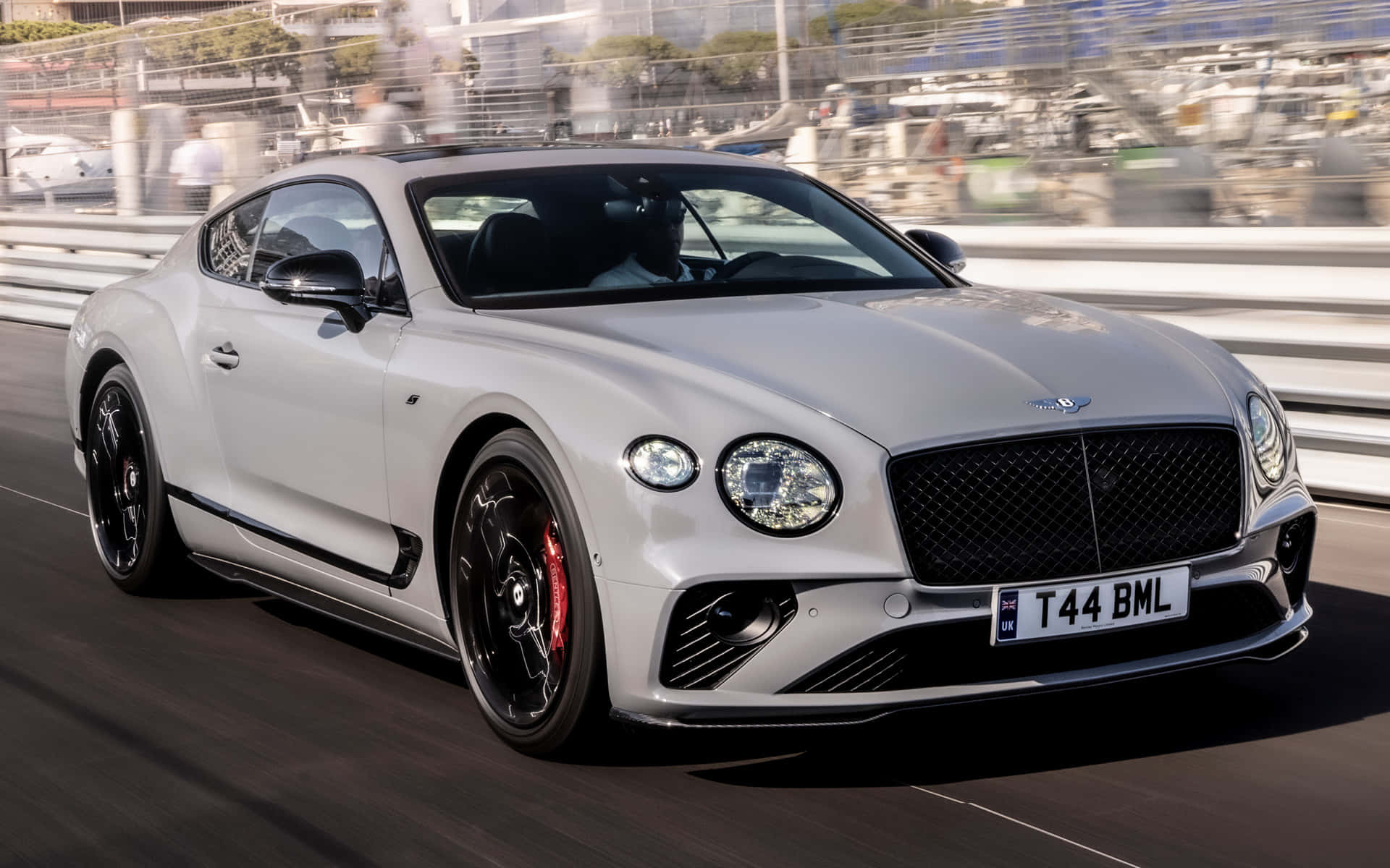 Bentley Continental Gt 桌布 壁紙 — 一台流線型的銀色賓利 Continental GT 在賽道上疾馳，背景是模糊的看台。