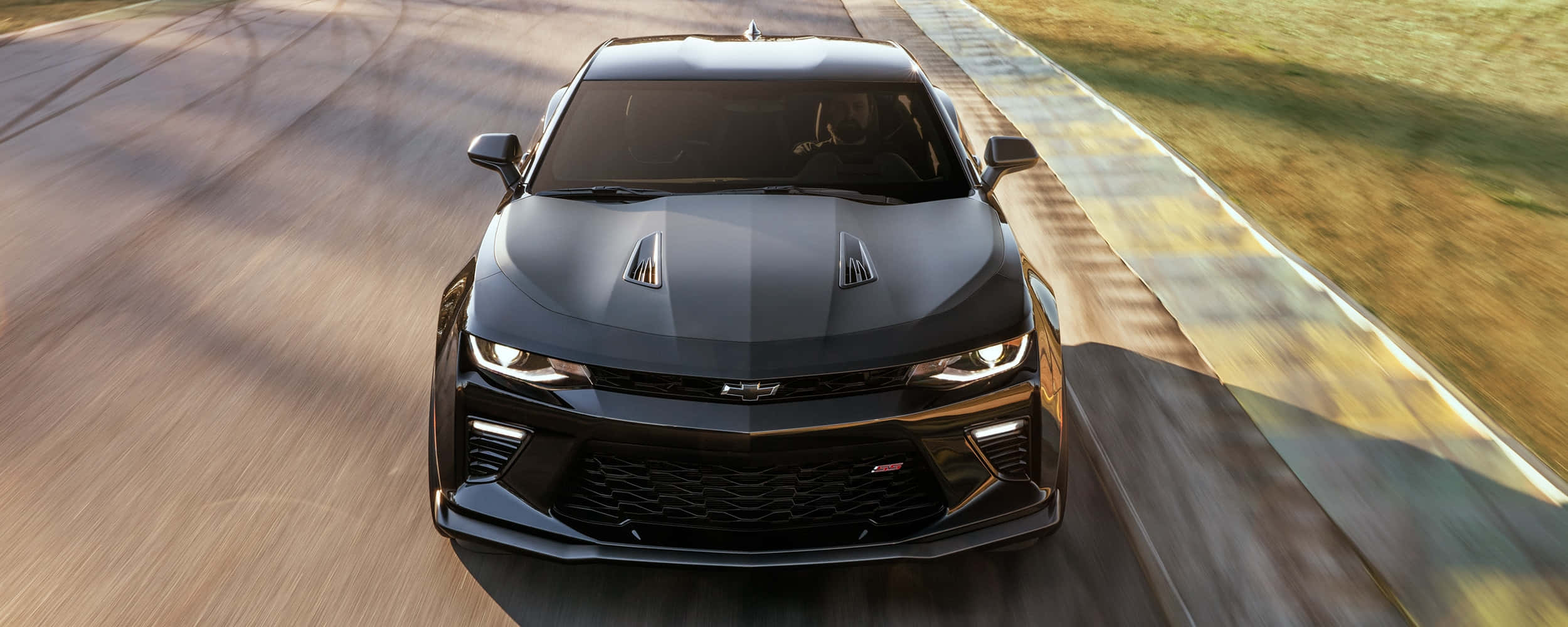 Cool Camaro 桌布 壁紙 — 一台流線型的黑色雪佛蘭Camaro在陽光明媚的賽道上疾馳，動態模糊效果強調了速度。
