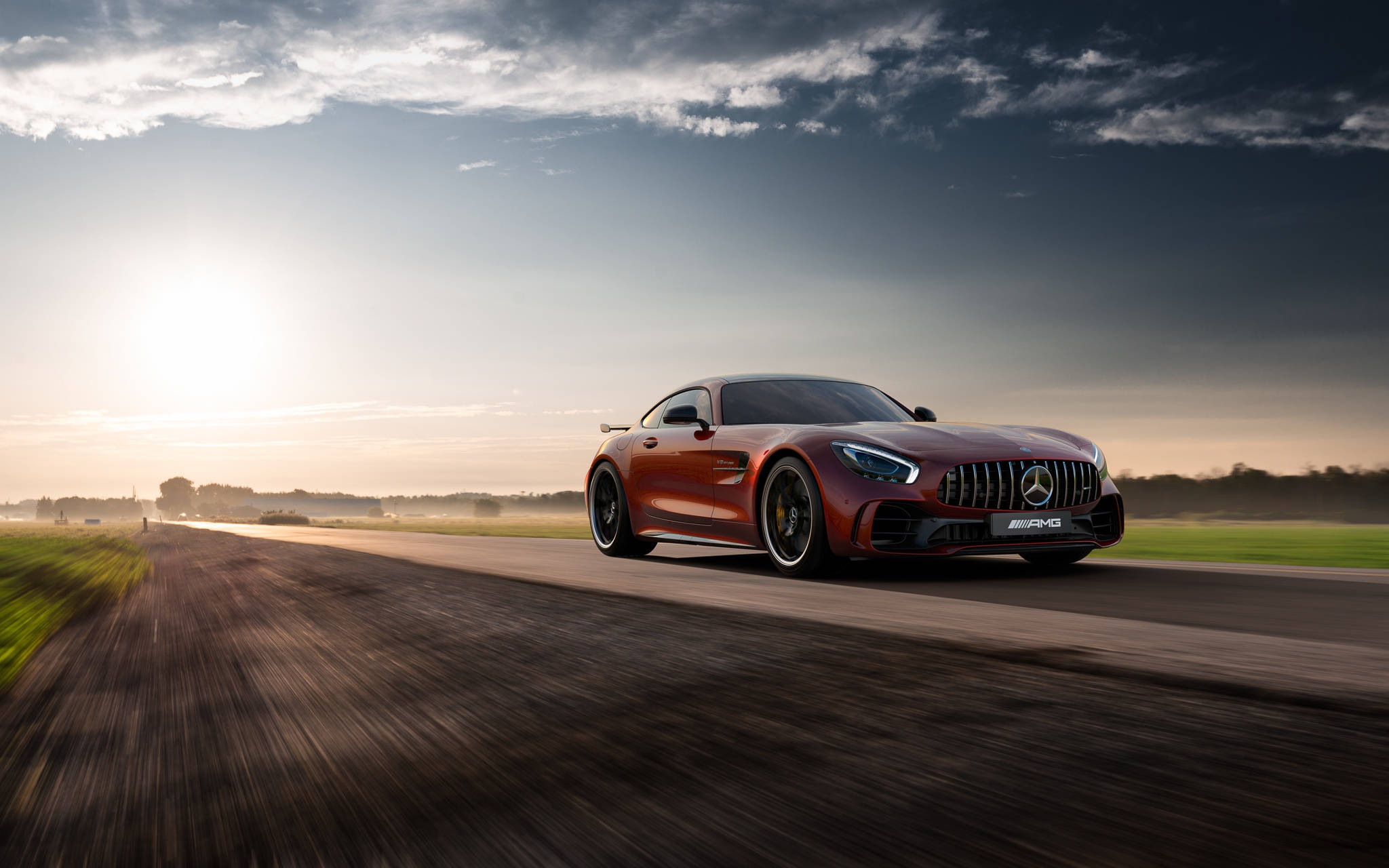 Gtr 桌布 壁紙 — 一台流線型紅色Mercedes-AMG GT R在日落時分沿鄉村道路疾馳，帶有動態模糊和戲劇性的雲層。