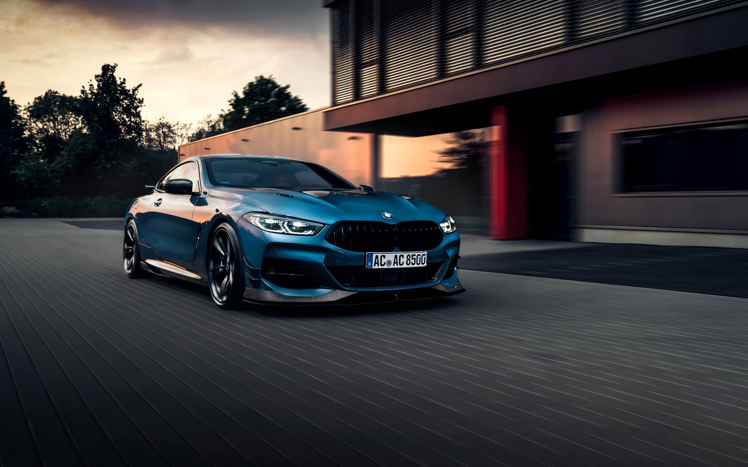 m 桌布 壁紙 — 一台流線型藍色BMW M8 Coupe在黃昏時高速駛過一棟現代建築，路上帶有動態模糊效果。