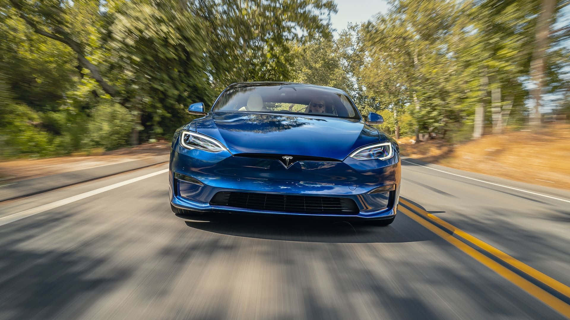 Hybrid Car 桌布 壁紙 — 一台流線型藍色Tesla Model S在綠樹成蔭的道路上飛馳，動態模糊效果突顯其速度。
