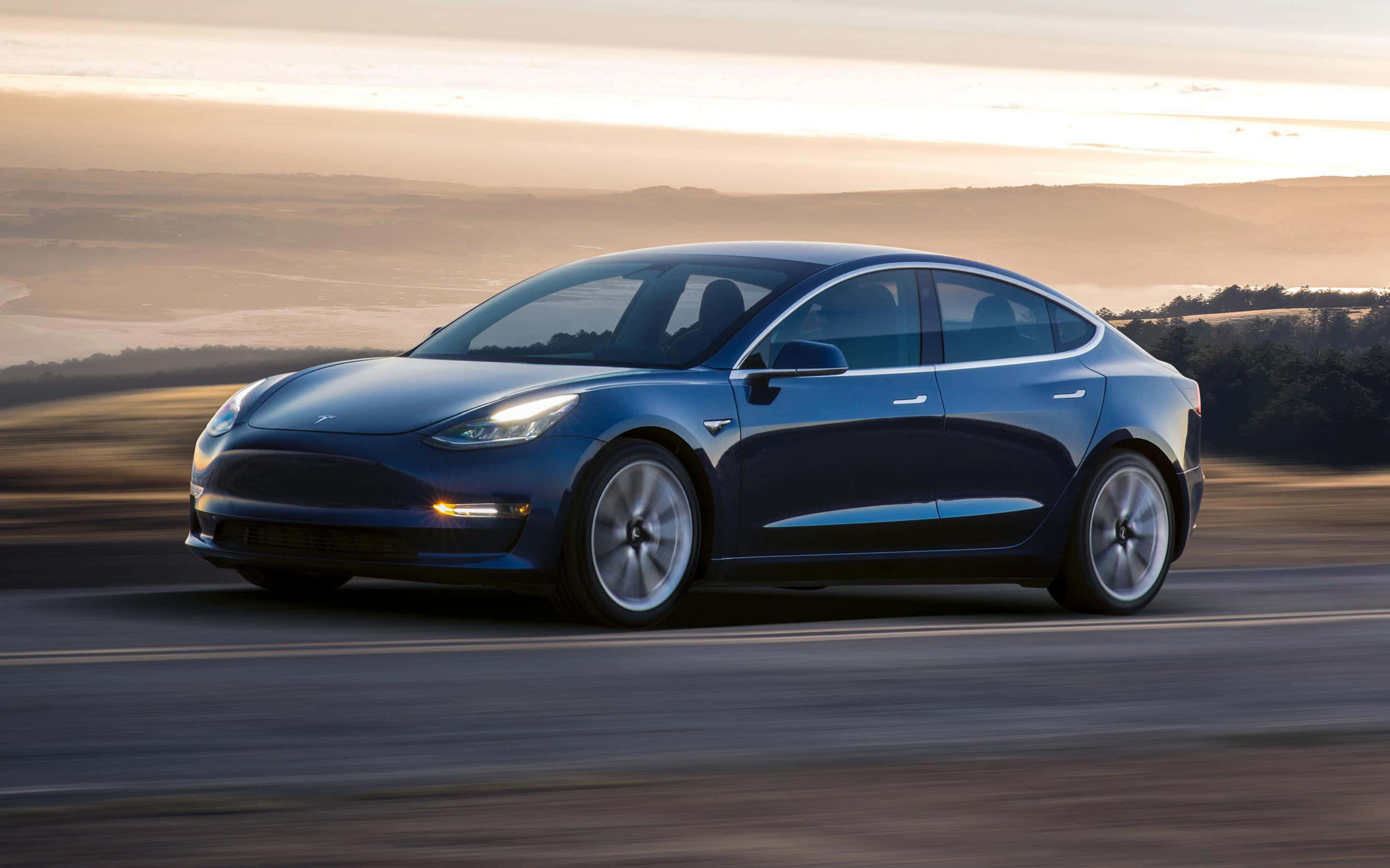 Tesla Model 3 桌布 壁紙 — 一台流線型藍色Tesla Model 3在黃金時段沿著蜿蜒的道路行駛，背景是模糊的山丘。