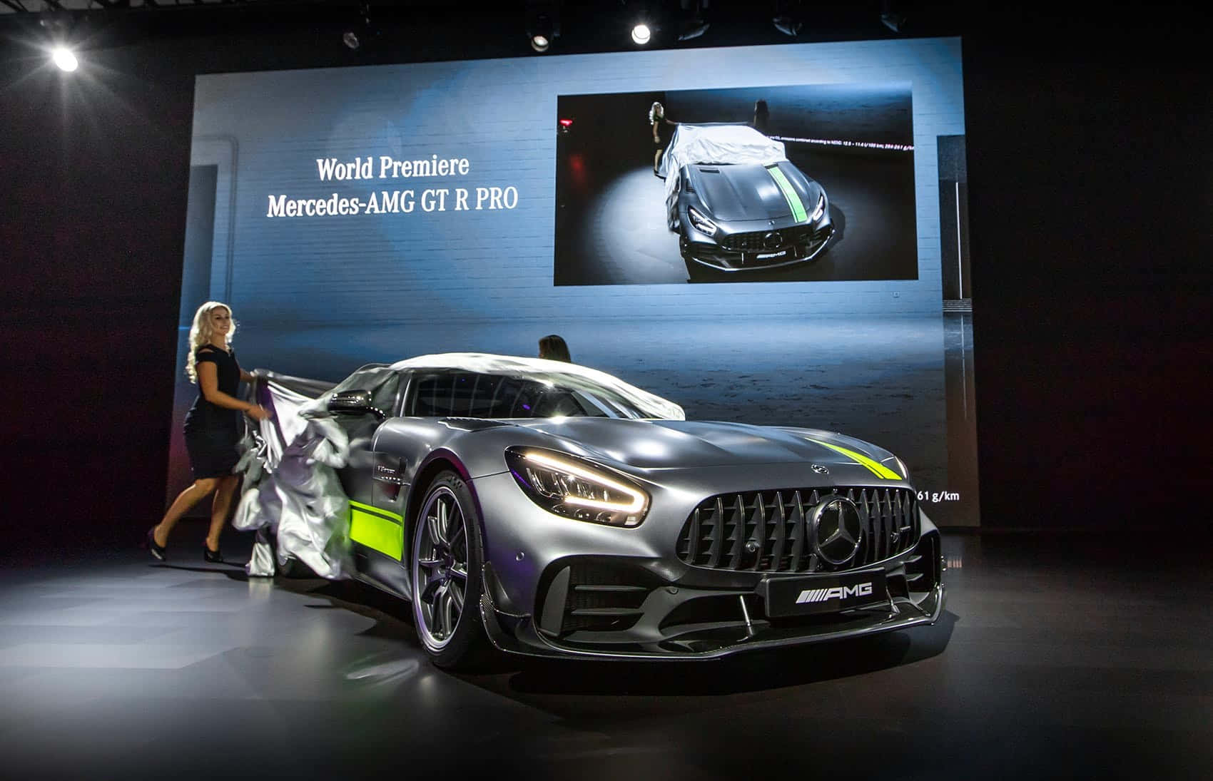 汽車 桌布 壁紙 — 一台流線型銀色 Mercedes-AMG GT R PRO 在黑暗舞台上，由一位女士在明亮聚光燈下揭開車罩亮相。