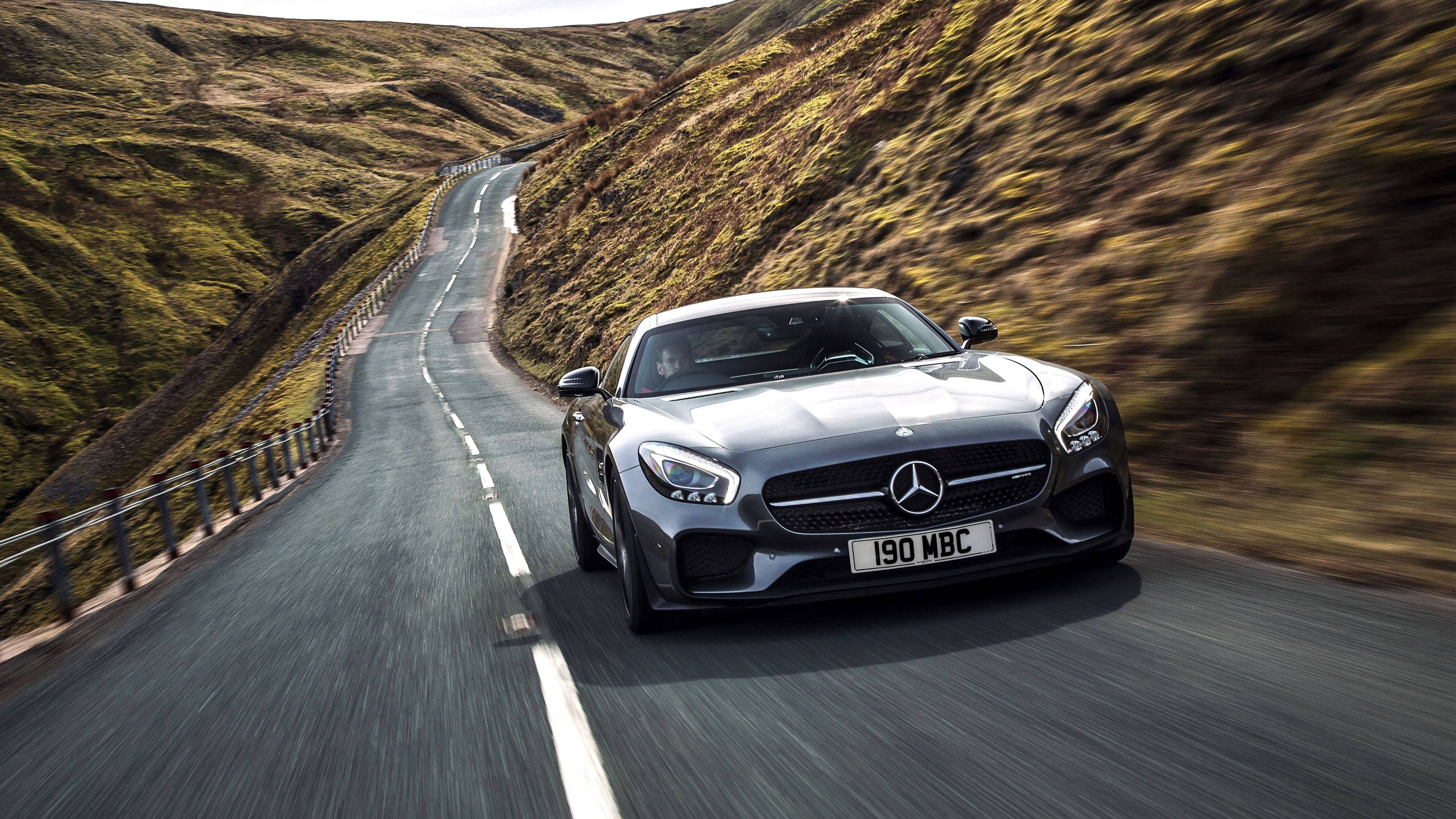 Cool Car 桌布 壁紙 — 一台流線型銀色 Mercedes-AMG GT S 沿著蜿蜒的山路疾馳，兩旁模糊的綠色山丘一閃而過。