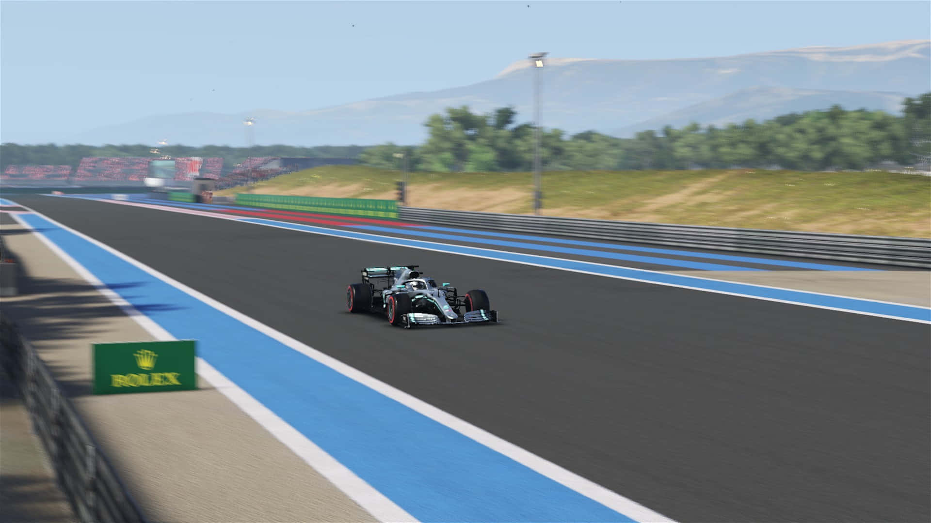 Race Track 桌布 壁紙 — 一台流線型銀色一級方程式賽車在陽光普照的賽道上奔馳，賽道有藍色路緣，遠處有綠色山丘，天空晴朗。