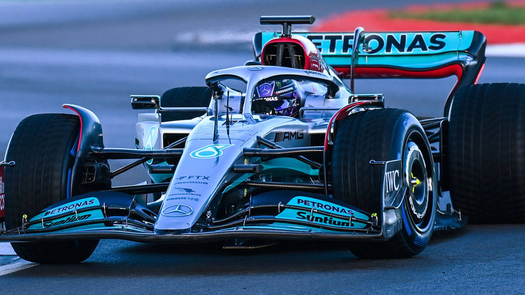F1 桌布 壁紙 — 一台流線型銀色和青色賓士AMG馬石油一級方程式賽車在賽道上疾馳，帶有動態模糊效果和可見的贊助商標誌。