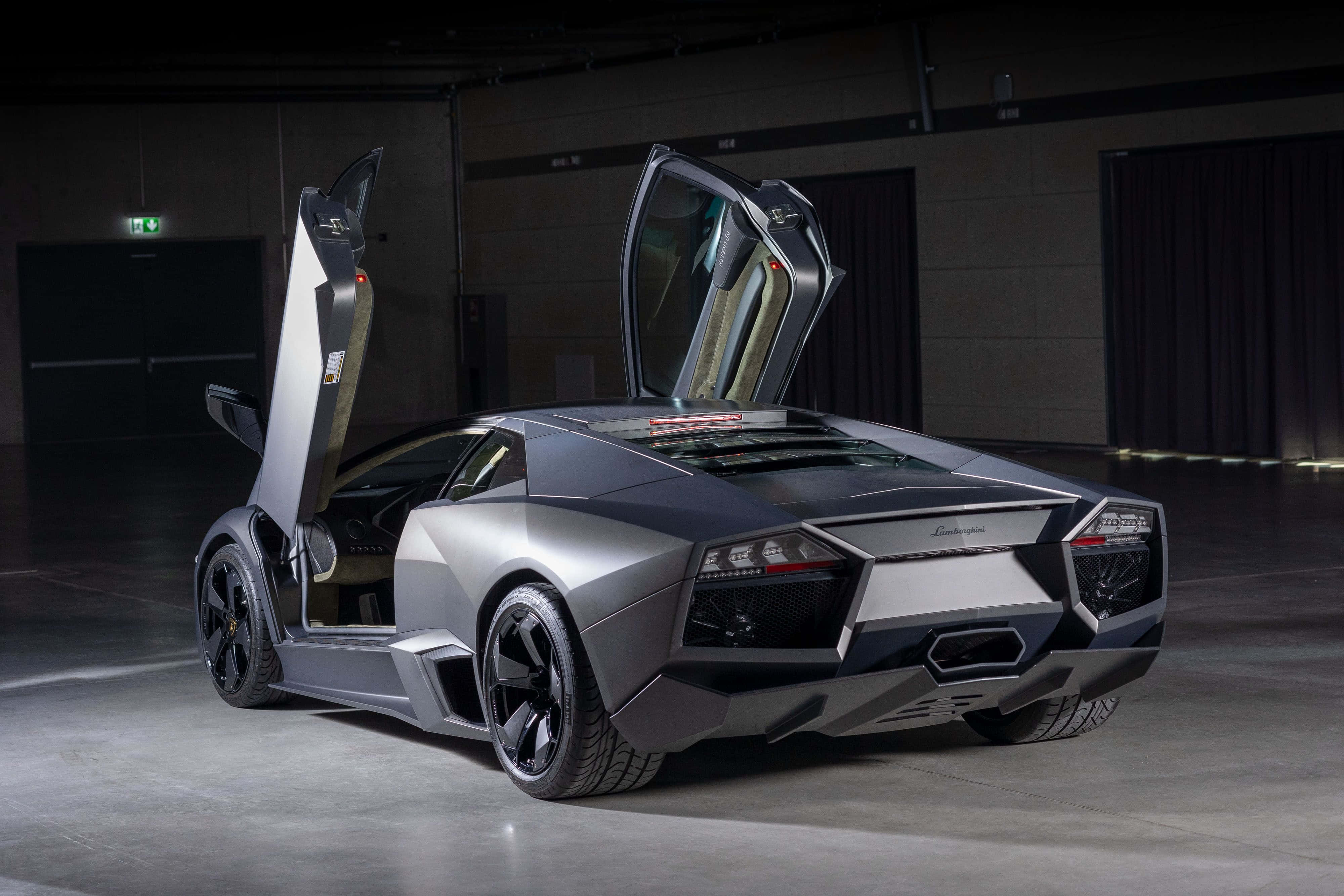Lamborghini Reventón 桌布 壁紙 — 一台流線型銀色藍寶堅尼Reventon，剪刀門打開，停在燈光昏暗的工業車庫中。