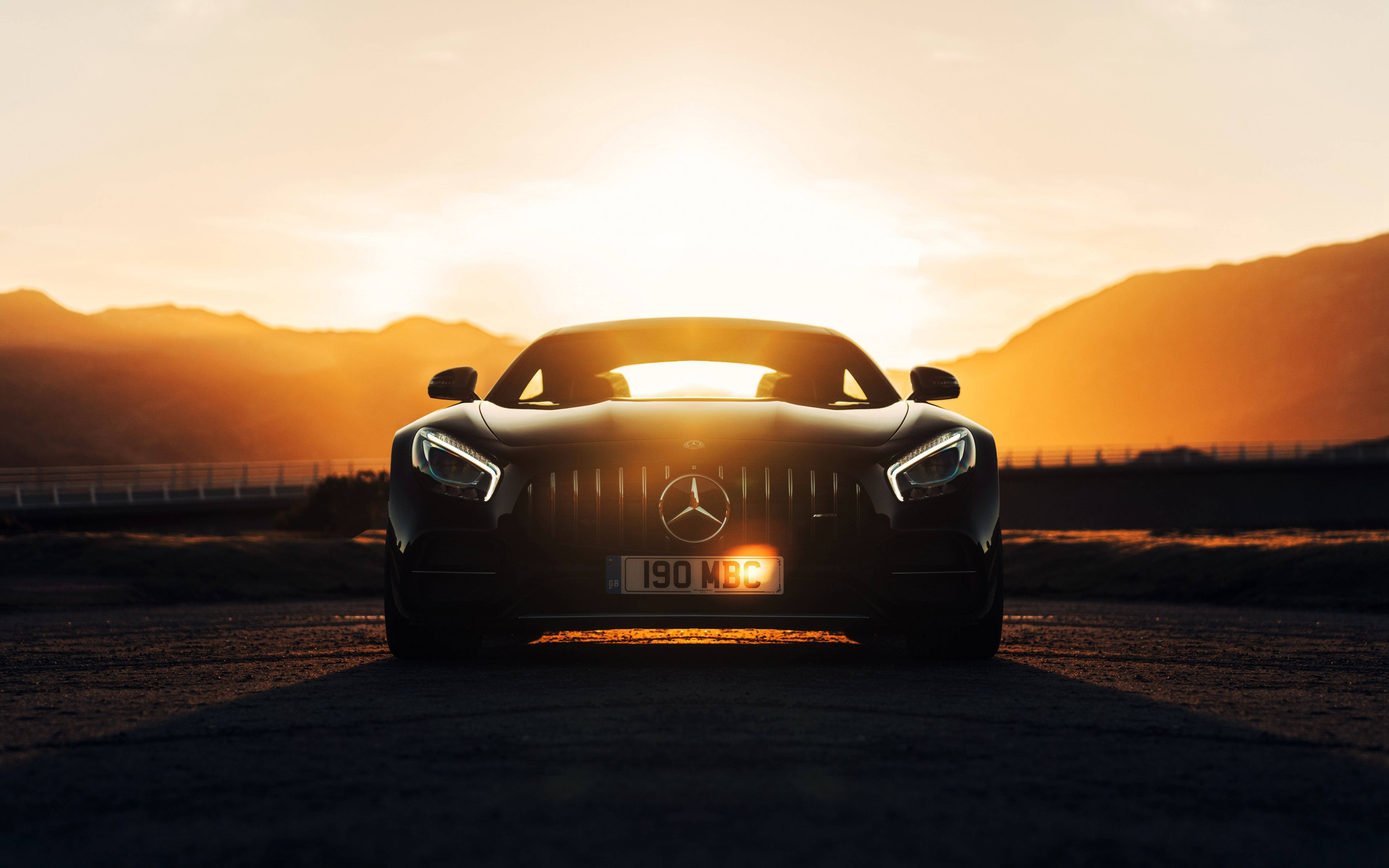 跑車 桌布 壁紙 — 一台流線型黑色 Mercedes-AMG GT 跑車在日落時面向鏡頭，金色光芒在水箱護罩和頭燈後方閃耀。