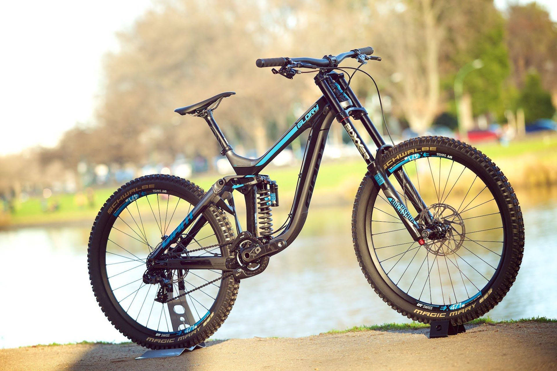 Mountain Bike 桌布 壁紙 — 一台流線型黑色和藍色全避震登山車，在柔和日光下靜立於寧靜湖邊。