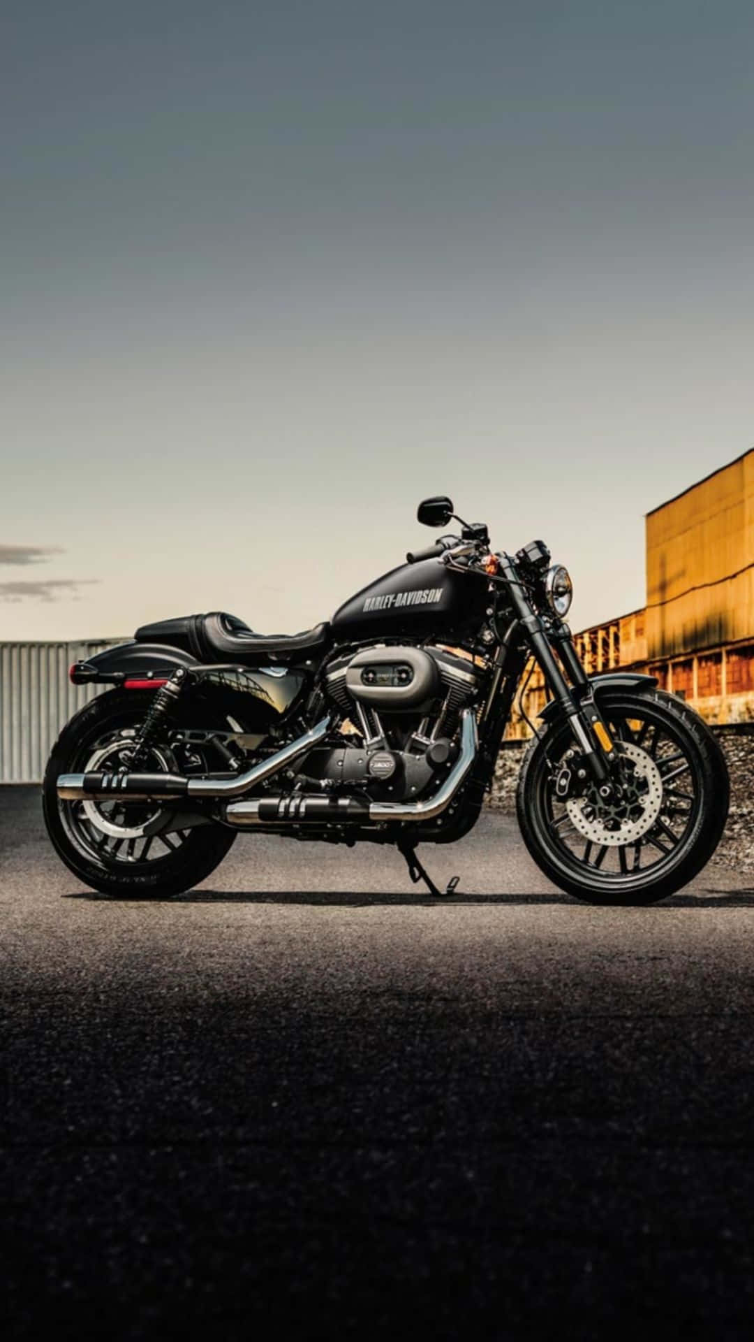 Harley Davidson HD 桌布 壁紙 — 一台流線型黑色哈雷機車在柔和的金色日落天空下，佇立在柏油路面上。
