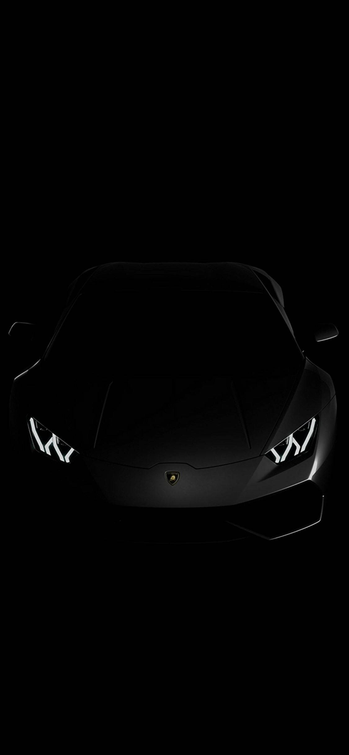 black apple iPhone 桌布 壁紙 — 一台流線型黑色藍寶堅尼跑車，在漆黑一片的虛空中，散發出銳利的白色頭燈光芒。
