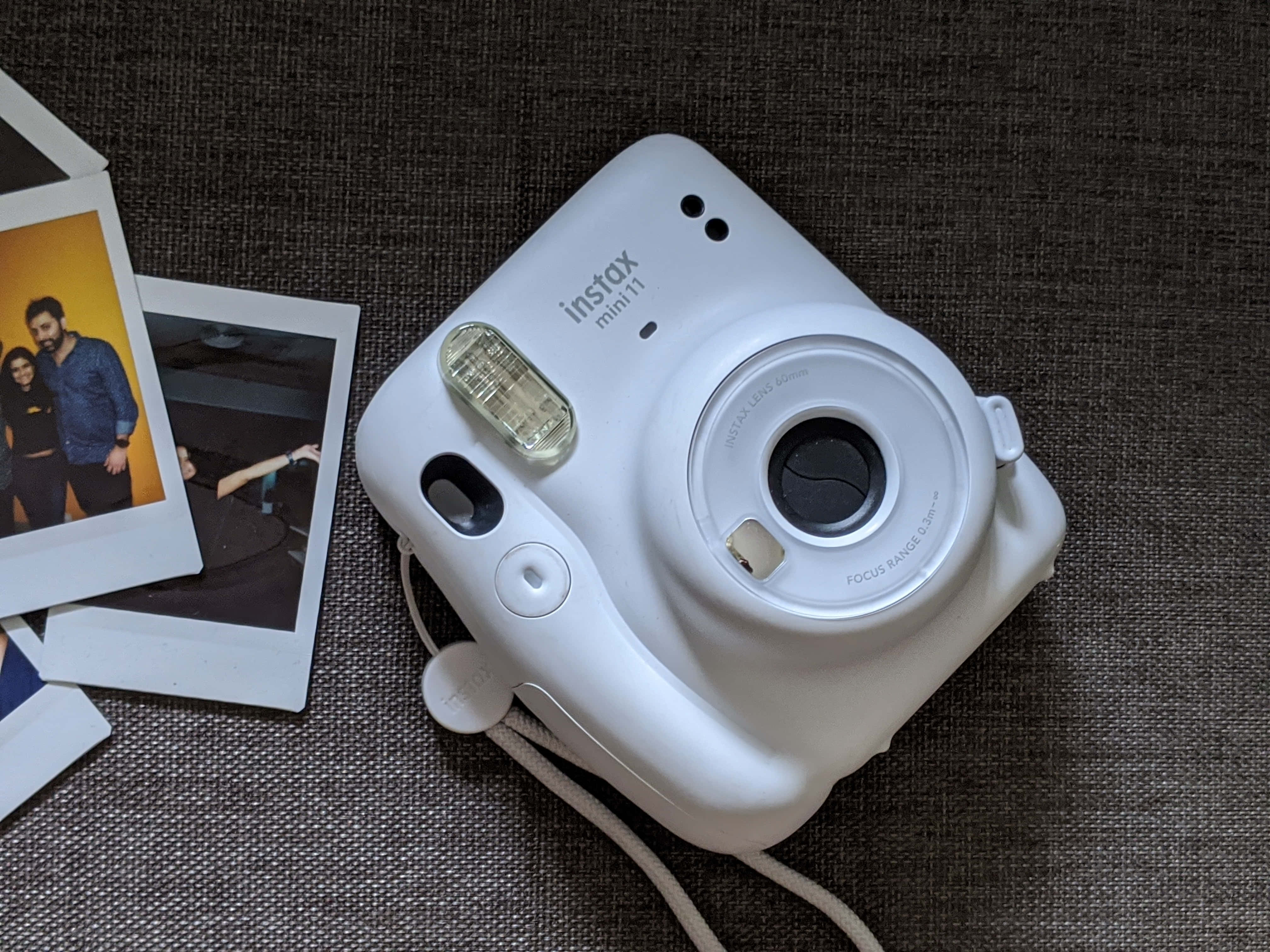 Photograph 桌布 壁紙 — 一台白色 Fujifilm Instax Mini 11 即時相機放置在帶有紋理的灰色布料上，旁邊散落著即時照片。