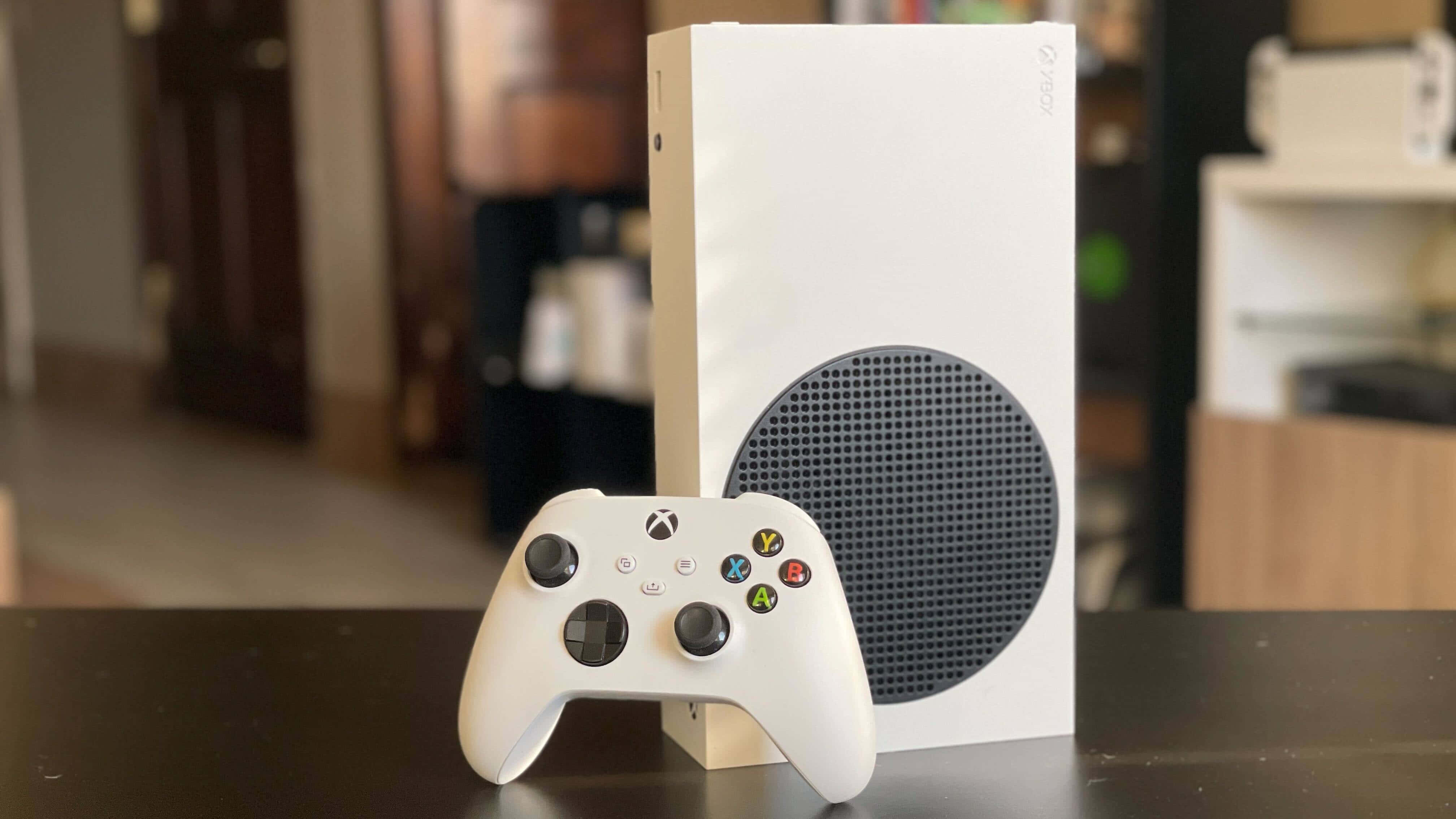 Xbox 桌布 壁紙 — 一台白色 Xbox Series S 主機和手把放在深色桌子上，背景為模糊的室內環境。