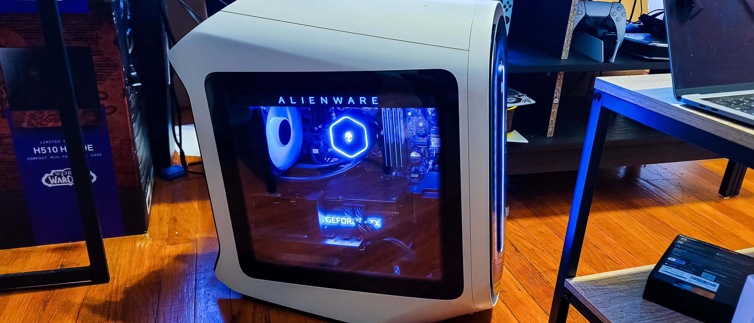 外星人 桌布 壁紙 — 一台白色Alienware遊戲電腦，帶有藍色內部照明，放在木地板上，旁邊有筆記型電腦和遊戲配件。
