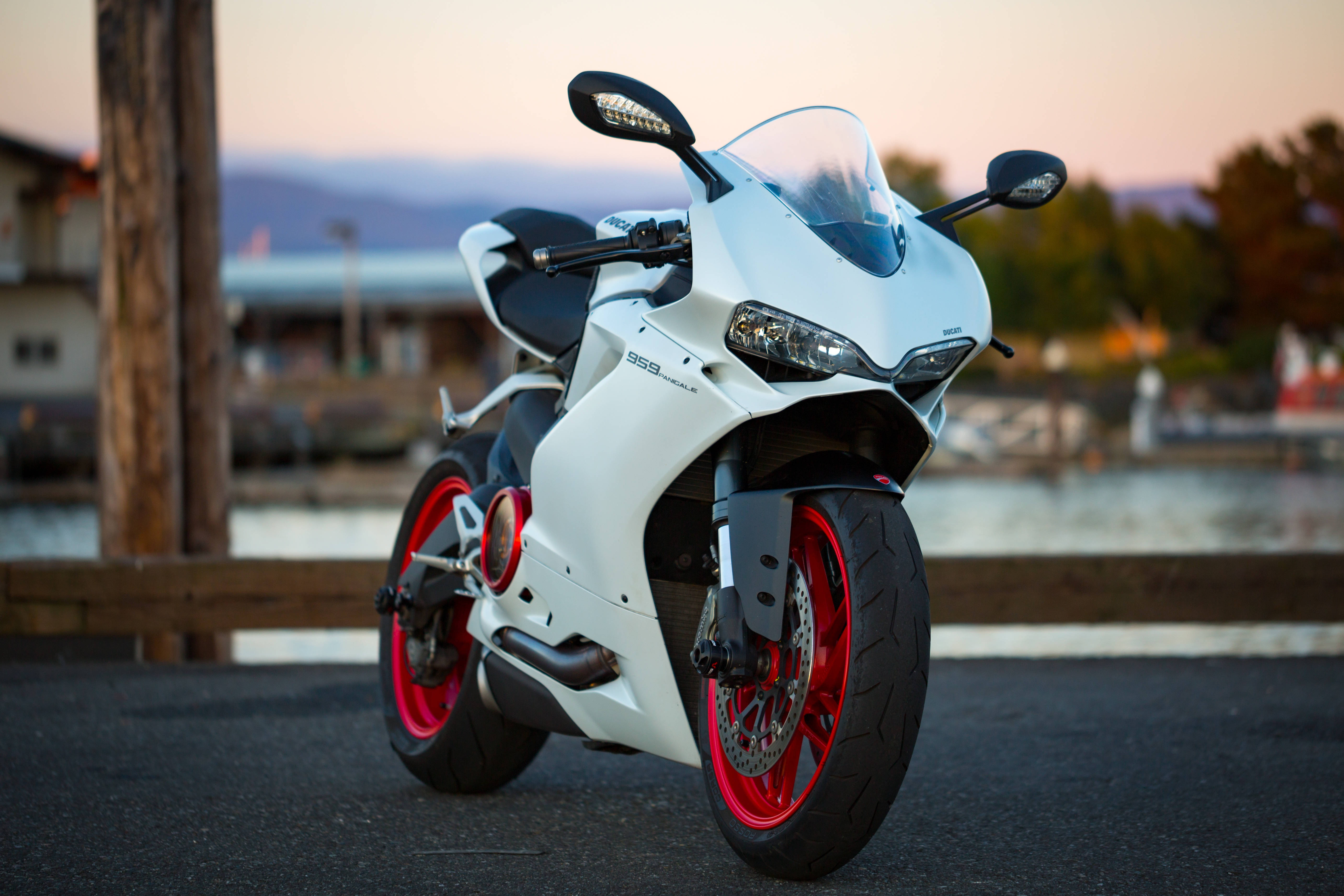  壁紙 — 一台白色Ducati 959 Panigale摩托車，紅色輪圈，停放在日落時分近水的柏油路上。