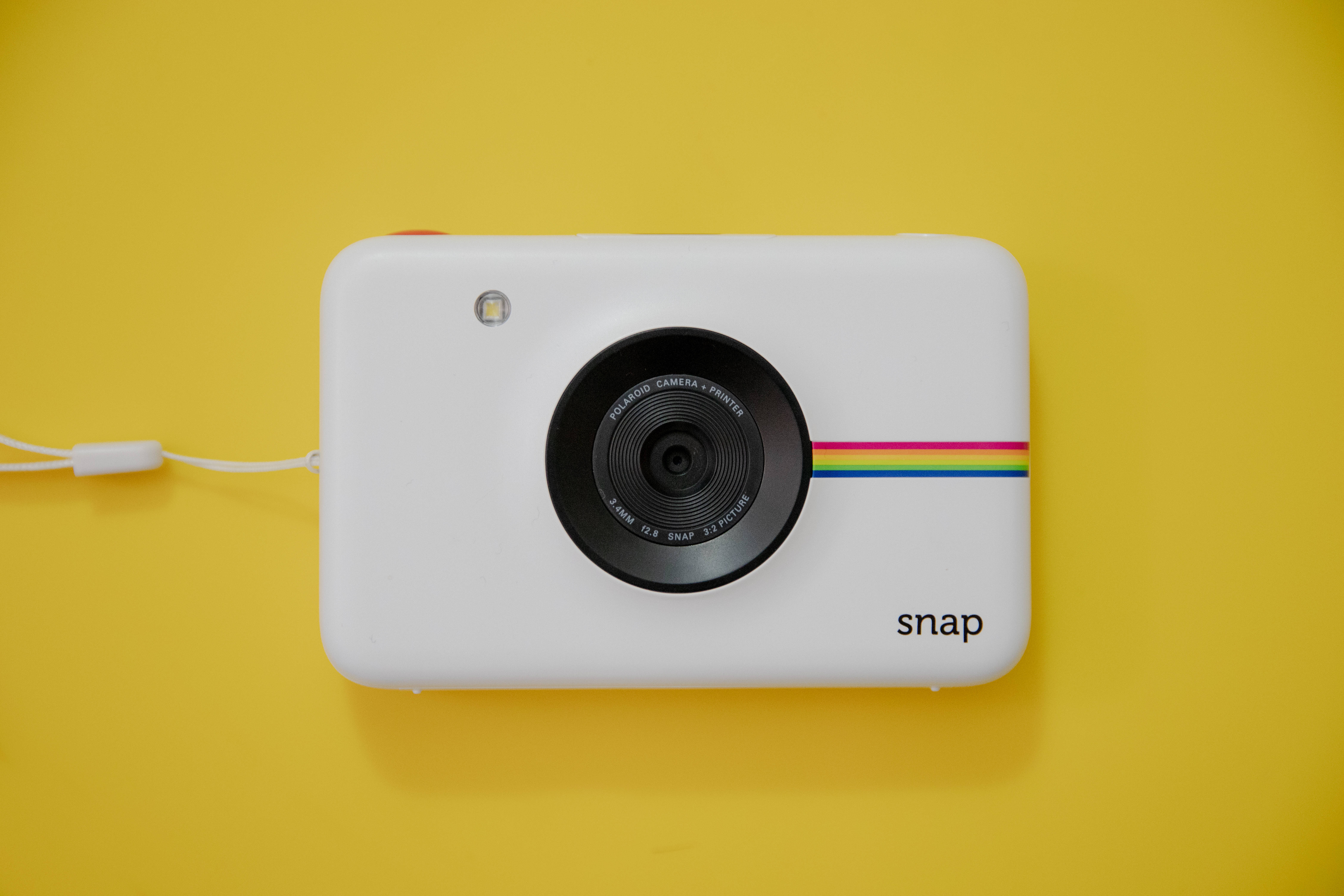 Webcam 桌布 壁紙 — 一台白色Polaroid Snap相機帶有彩虹條紋，居中放置在亮黃色背景上。