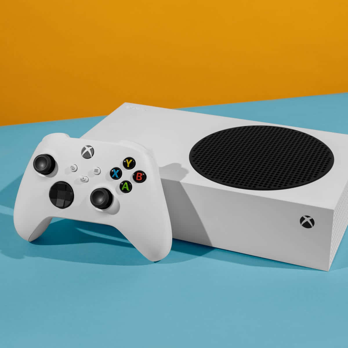 Xbox 桌布 壁紙 — 一台白色Xbox主機和手把放在藍色表面上，背景為鮮豔的橙色。