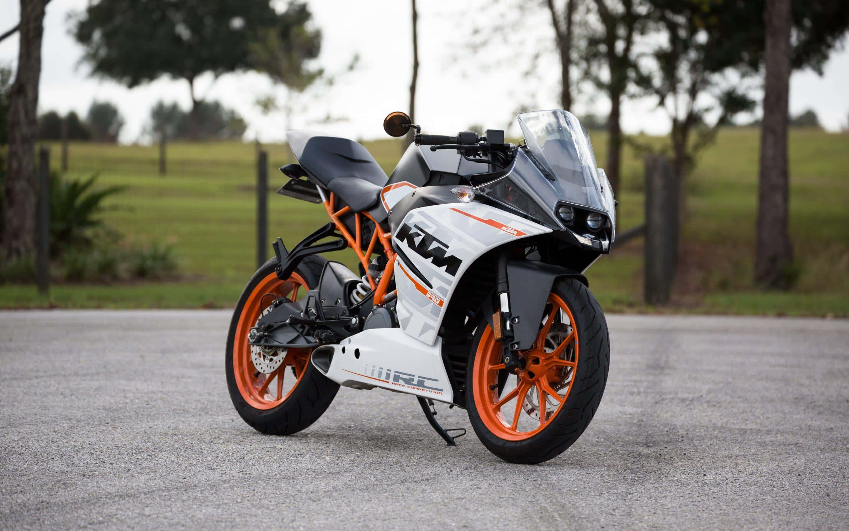 機車 桌布 壁紙 — 一台白色和橙色的KTM RC機車，時尚地停在碎石路上，背景有樹木和草地。