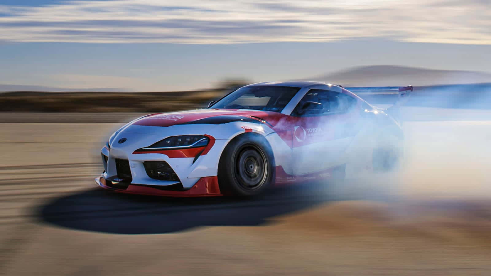 紅色和白色的豐田Supra在塵土飛揚的賽道上漂移，伴隨著煙霧。 — Toyota Supra Mk4 壁紙