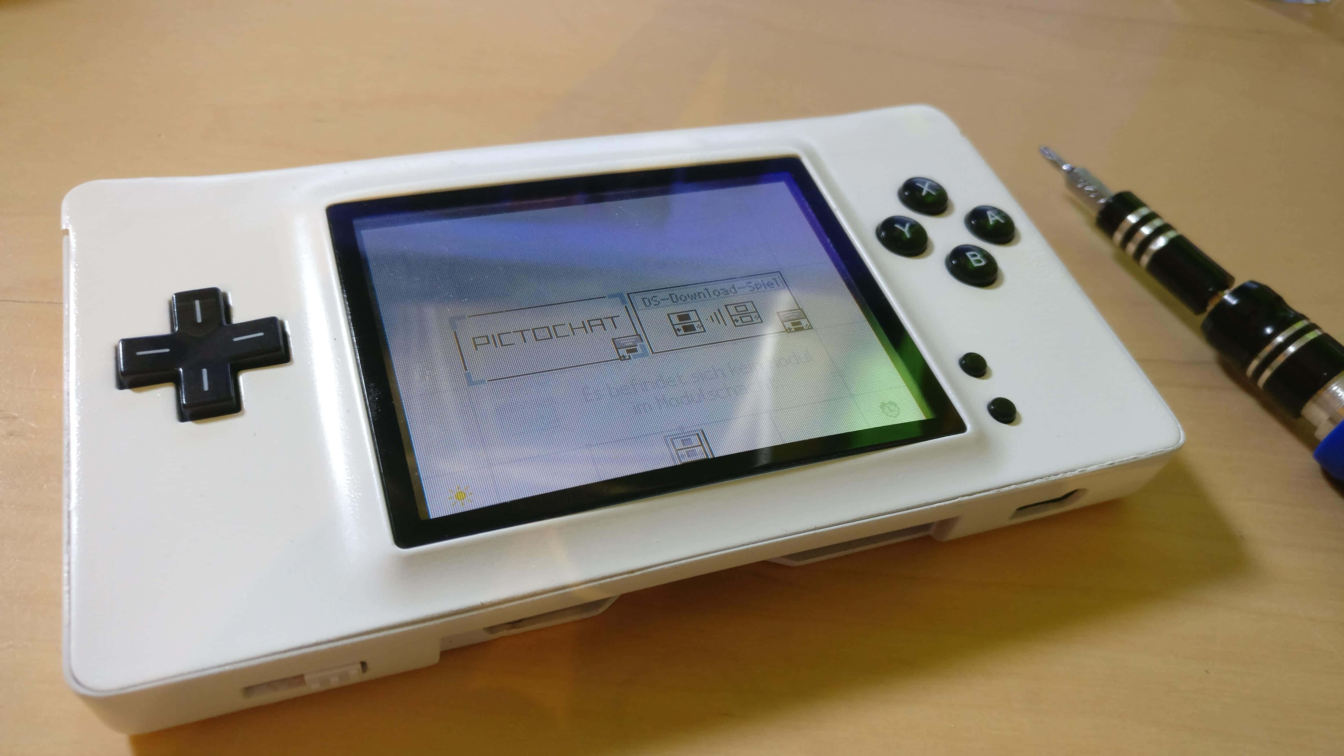 4K Gaming Consoles 桌布 壁紙 — 一台白色手持遊戲機，螢幕顯示PictoChat，放在木桌上，旁邊有一支觸控筆。