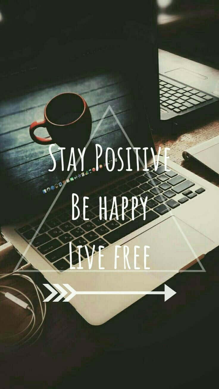Be Happy 桌布 壁紙 — 一台筆記型電腦在木桌上顯示勵志文字，旁邊有咖啡杯、電線和一支筆。