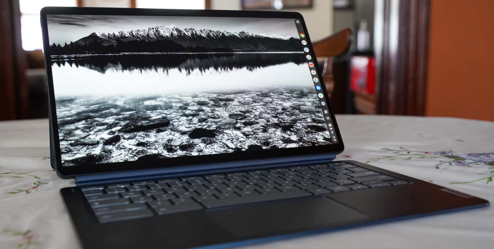 Chromebook 桌布 壁紙 — 一台筆記型電腦在花卉桌布上顯示單色山湖桌布，有雪覆蓋的山峰和冰冷的水面倒影。