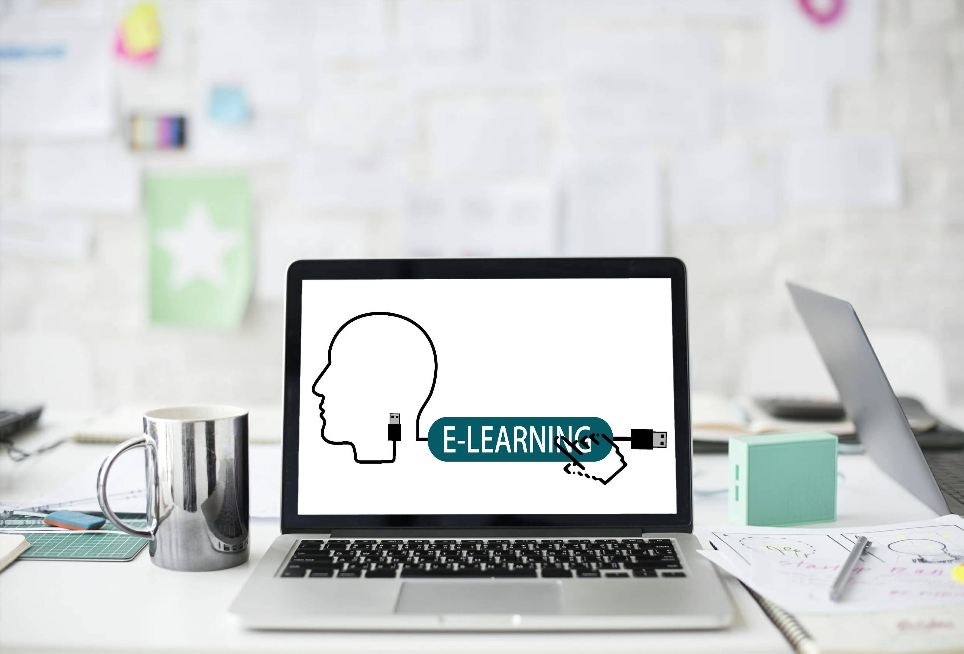 Learning 桌布 壁紙 — 一台筆記型電腦顯示一個頭部連接到電子學習電纜的圖形，整齊的桌子上有一個杯子和散落的筆記。