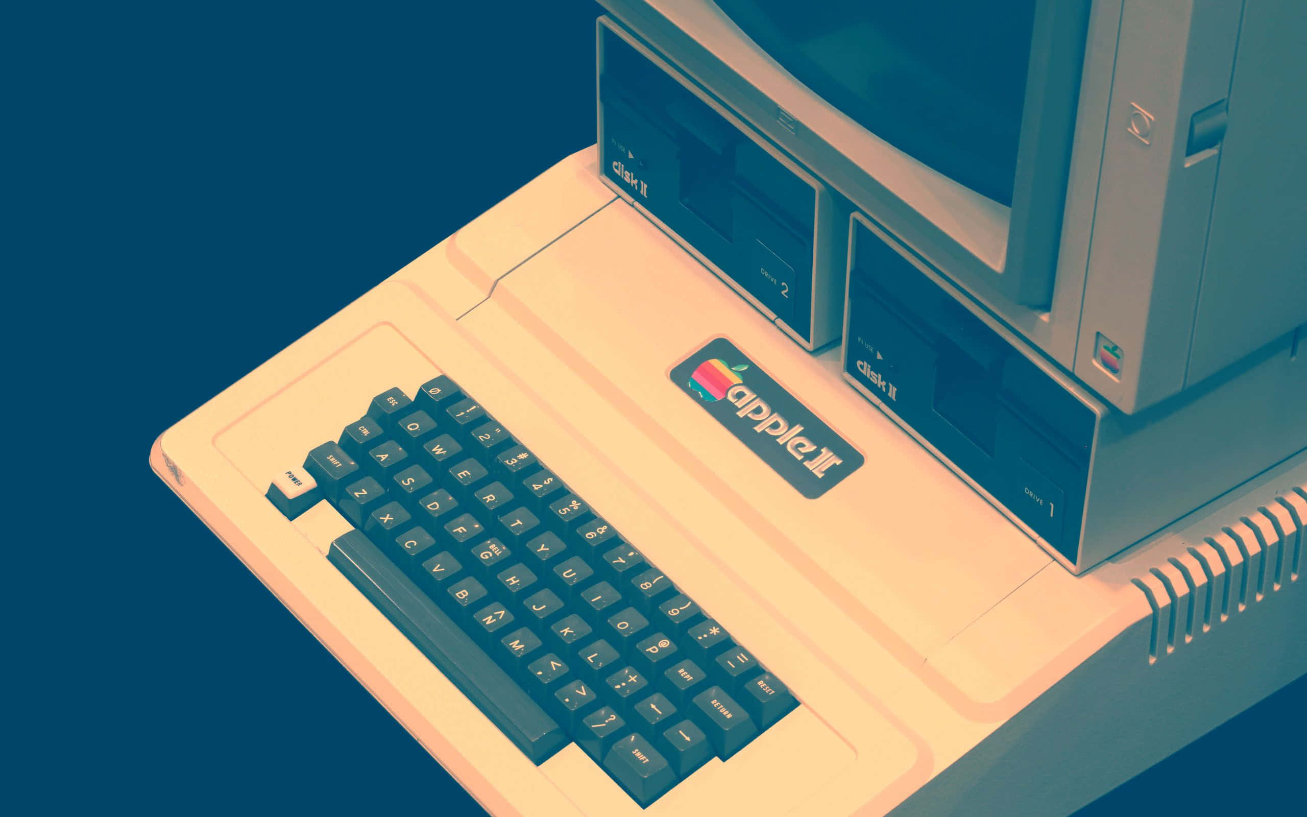 Old Pc 桌布 壁紙 — 一台米色外殼、深色鍵盤的復古Apple II電腦，傾斜放置在深藍色背景前。