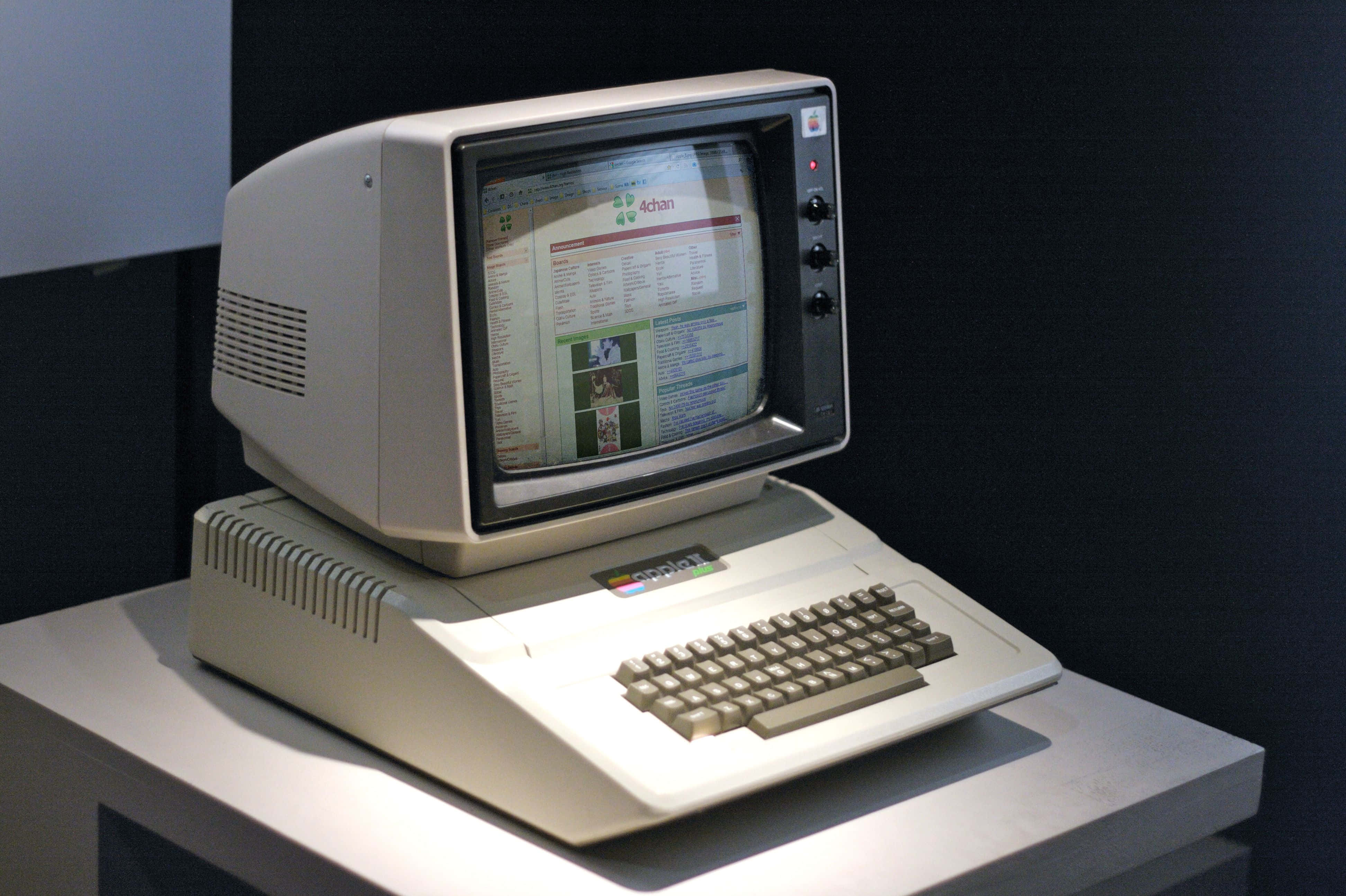 Old Pc 桌布 壁紙 — 一台米色復古電腦，配備CRT顯示器和內建鍵盤，放在展示座上，背景是深色牆壁。