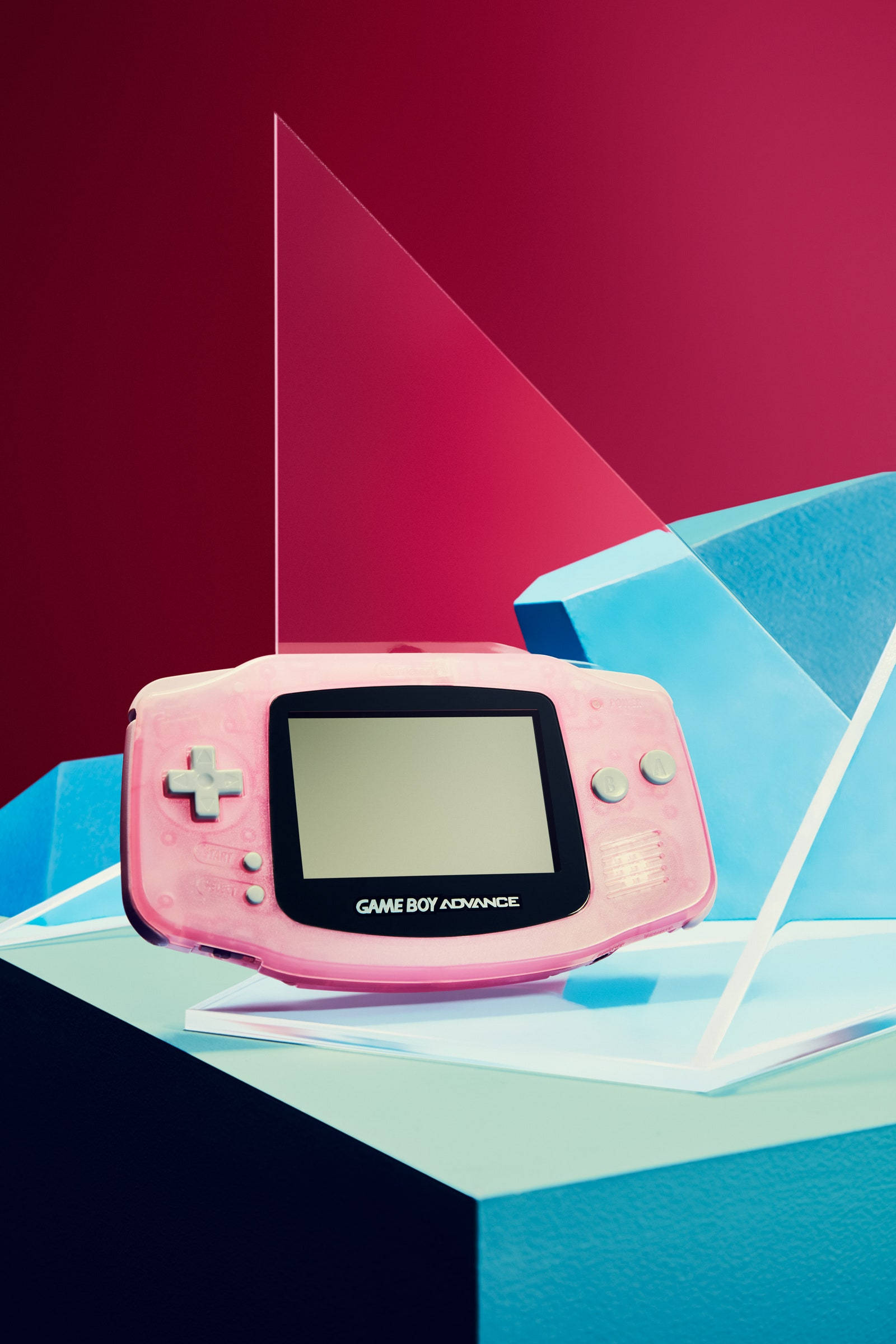game 桌布 壁紙 — 一台粉紅色 Game Boy Advance 放置在幾何藍色和黑色方塊上，背景為大膽的紅色。