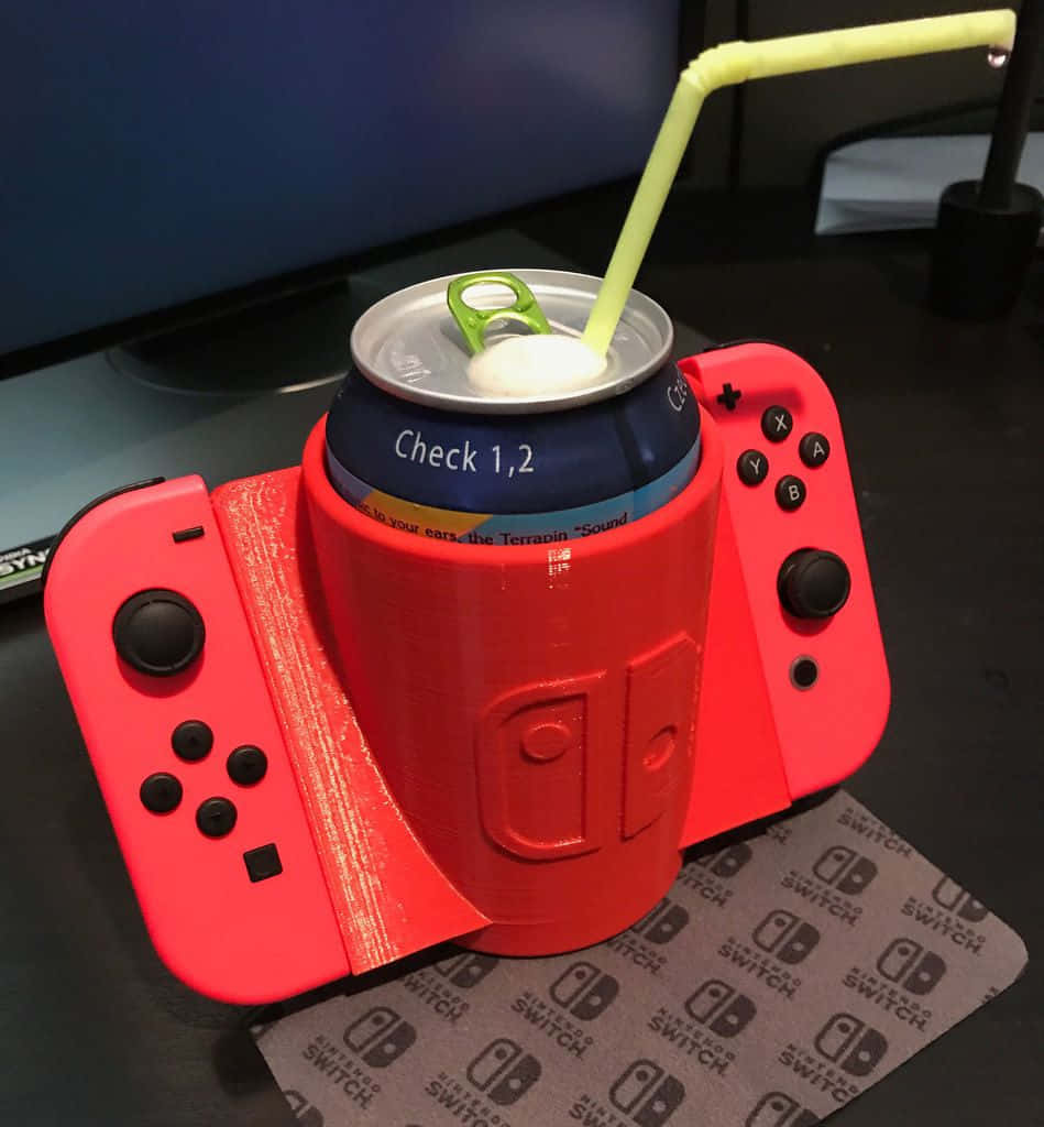 Gaming Accessories 桌布 壁紙 — 一台紅色Nintendo Switch主機被創意地改造成飲料架，用來放置附有吸管的汽水罐。