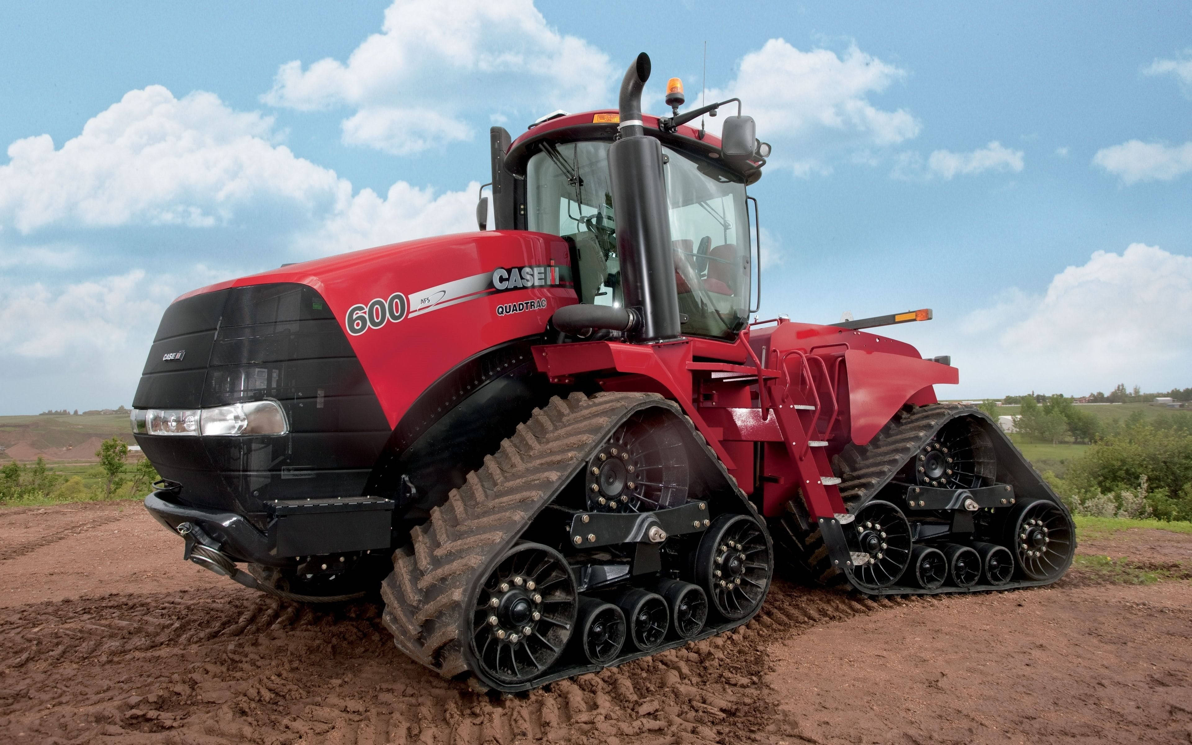 Farmer 桌布 壁紙 — 一台紅色的 Case IH Quadtrac 600 履帶拖拉機站在泥濘的地形上，頭頂是晴朗的藍天和蓬鬆的白雲。