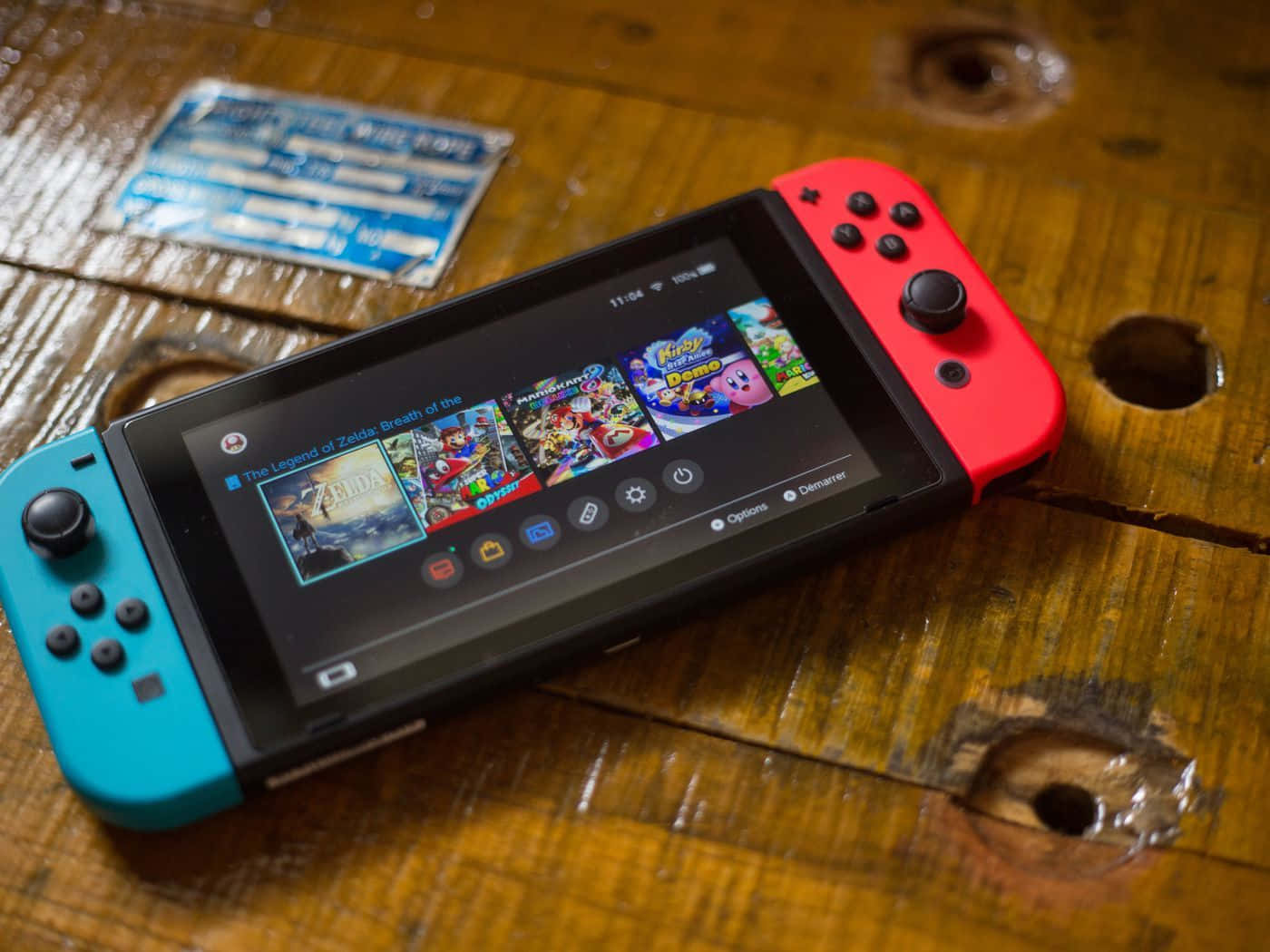 Gaming Consoles 桌布 壁紙 — 一台紅藍色Nintendo Switch放在風化的木桌上，顯示色彩繽紛的遊戲圖標。
